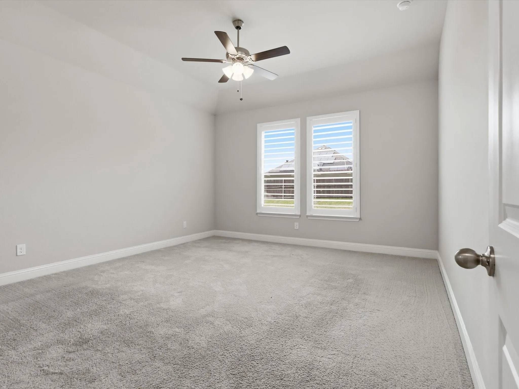 Spacious room featuring dual windows with plantation shutters, plush carpeting, a ceiling fan with integrated lighting, and neutral wall tones