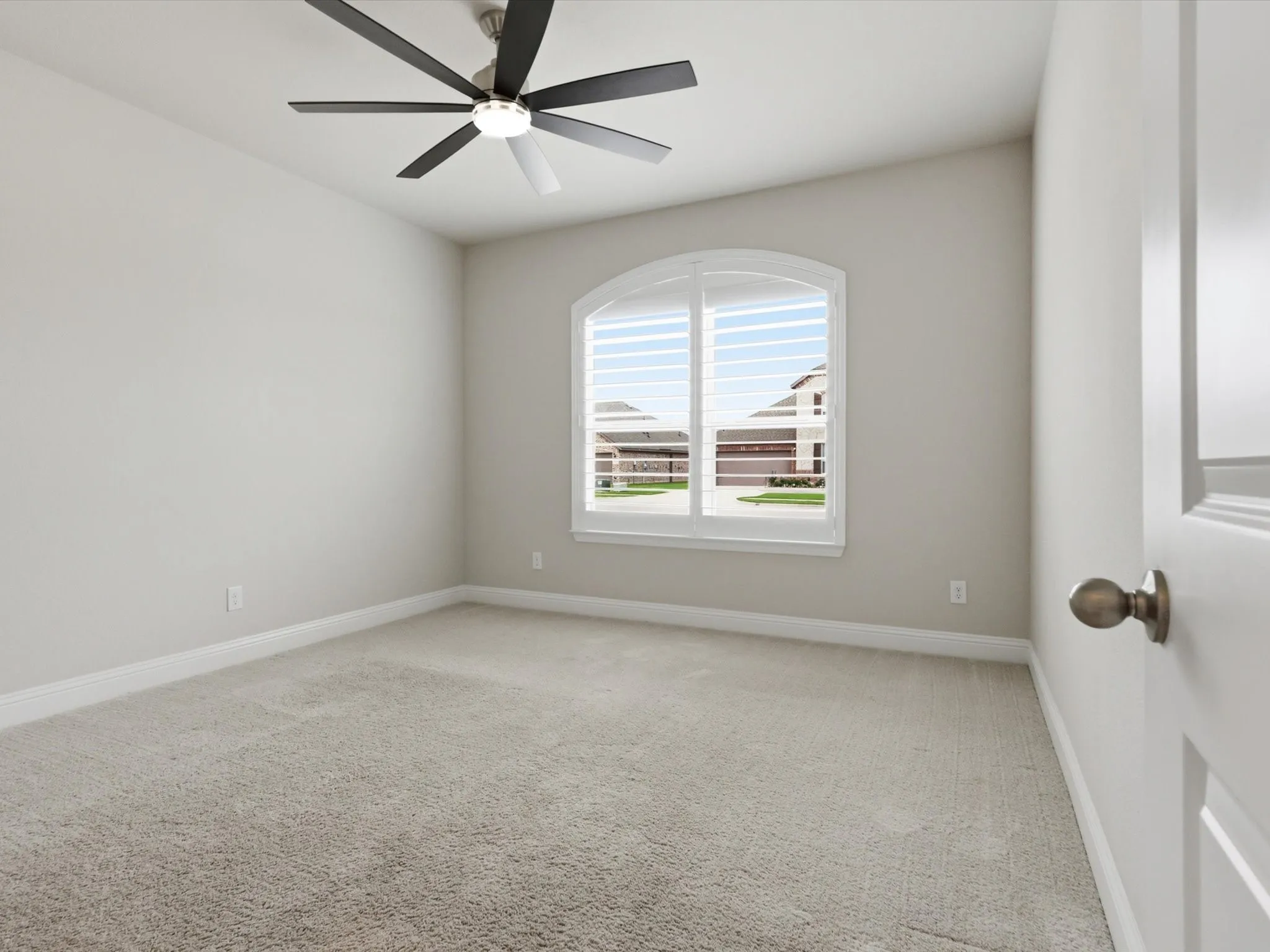 Carpeted room with a vaulted ceiling and an arched window featuring plantation shutters