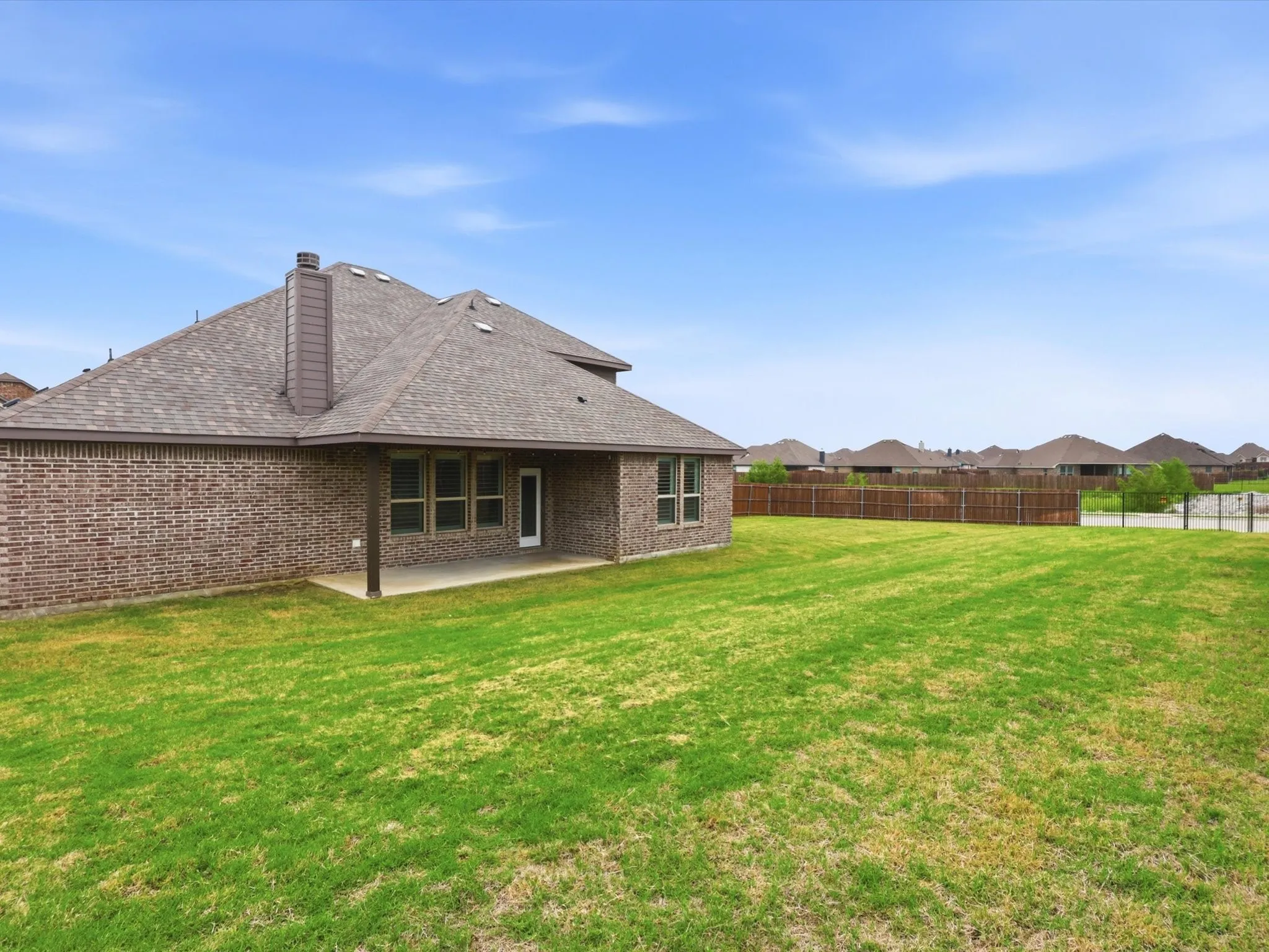 Spacious backyard featuring a covered patio with a concrete slab, brown brick exterior, multi-pane windows, and a shingled roof