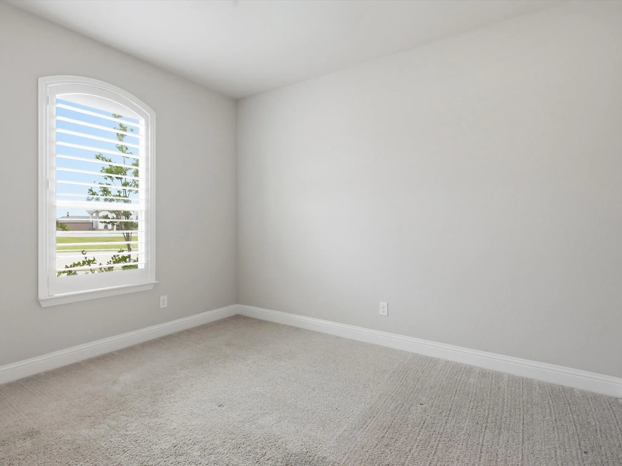 Arch-top window with plantation shutters, light gray wall paint, and gray carpeting