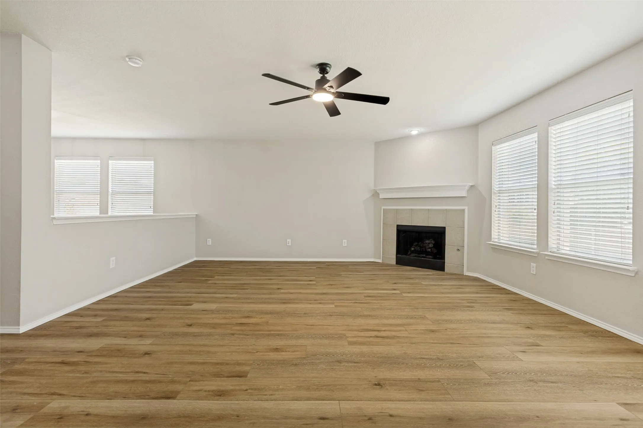 Spacious room featuring wood-finish flooring, a ceiling fan, and multiple windows with blinds