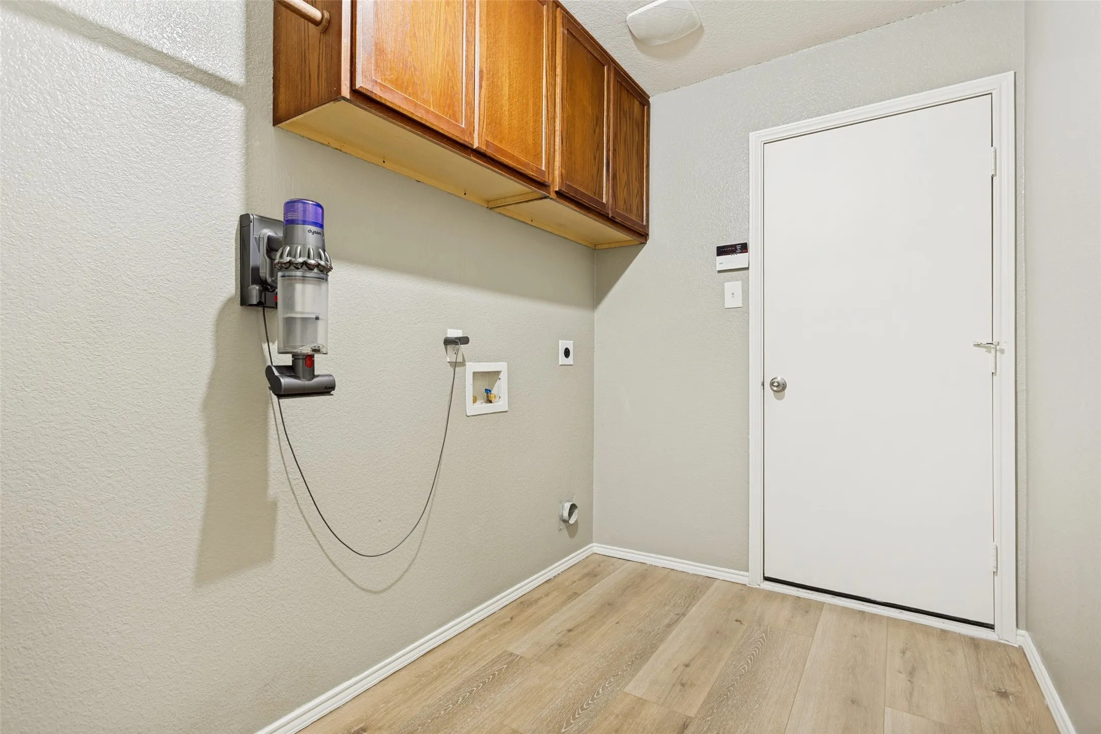Laundry area featuring wood-finish flooring, light gray walls, and upper cabinetry