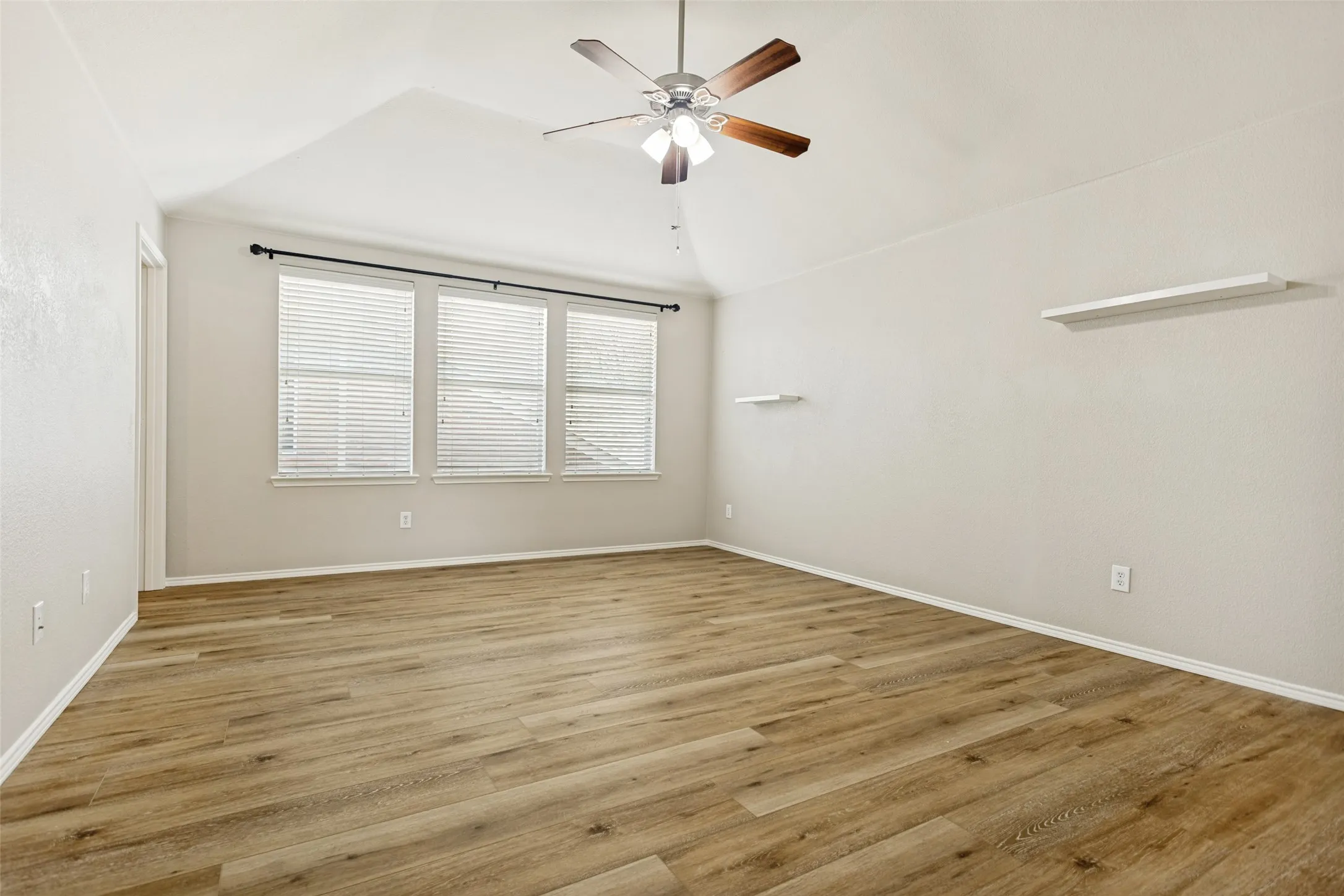 Spacious room featuring wood-finish flooring, vaulted ceiling, and a ceiling fan with integrated lighting