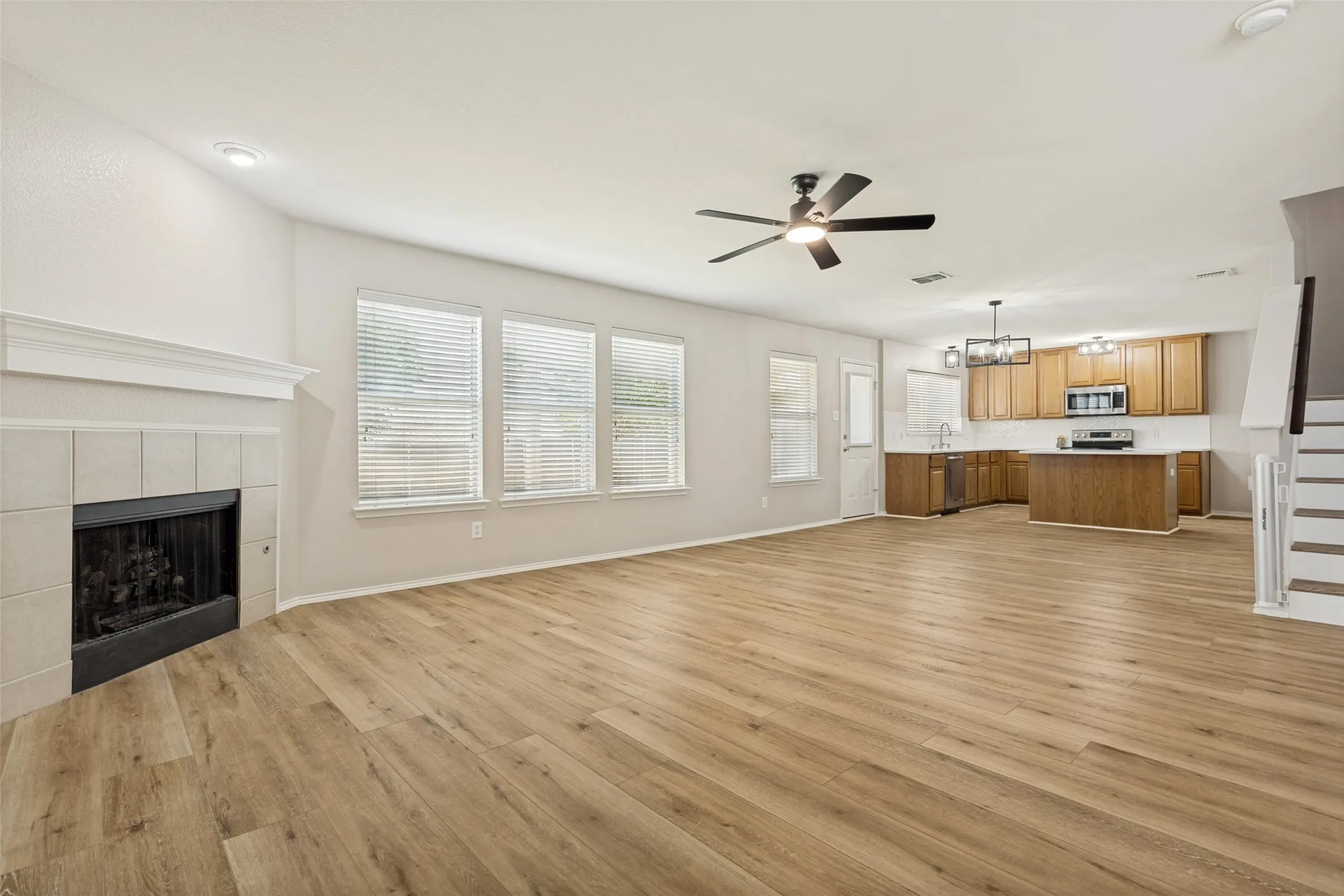 Spacious open-concept living area featuring wood-finish flooring, a tile-surround fireplace with a mantel, and multiple windows