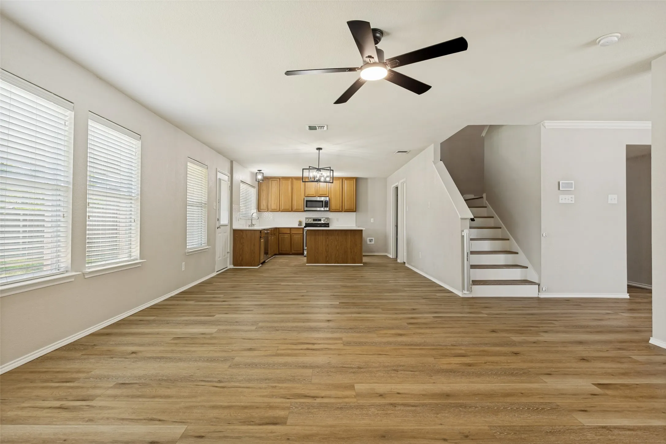 Spacious open-concept living area featuring wood-finish flooring, multiple windows, and a ceiling fan
