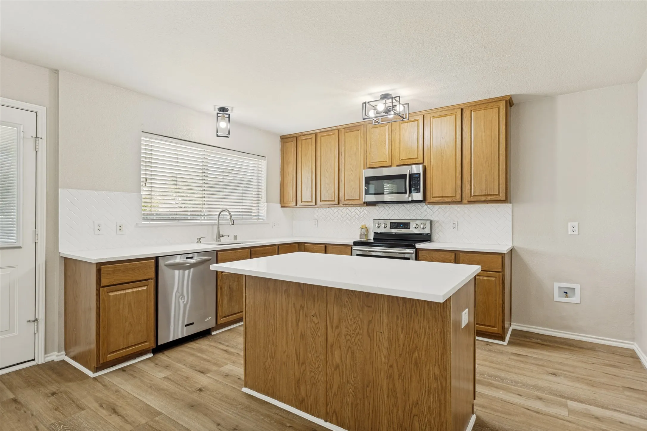 Kitchen featuring wood-finish flooring, a central island with a white countertop, and light wood cabinetry