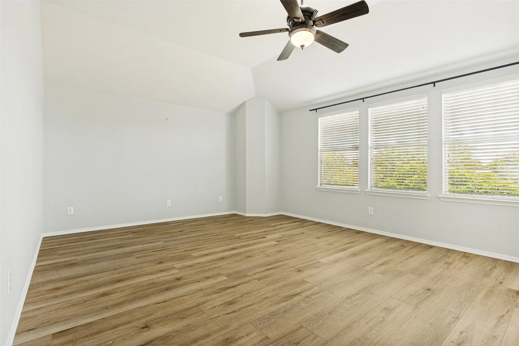 Spacious interior room featuring wood-finish flooring, a vaulted ceiling, and a ceiling fan with integrated lighting