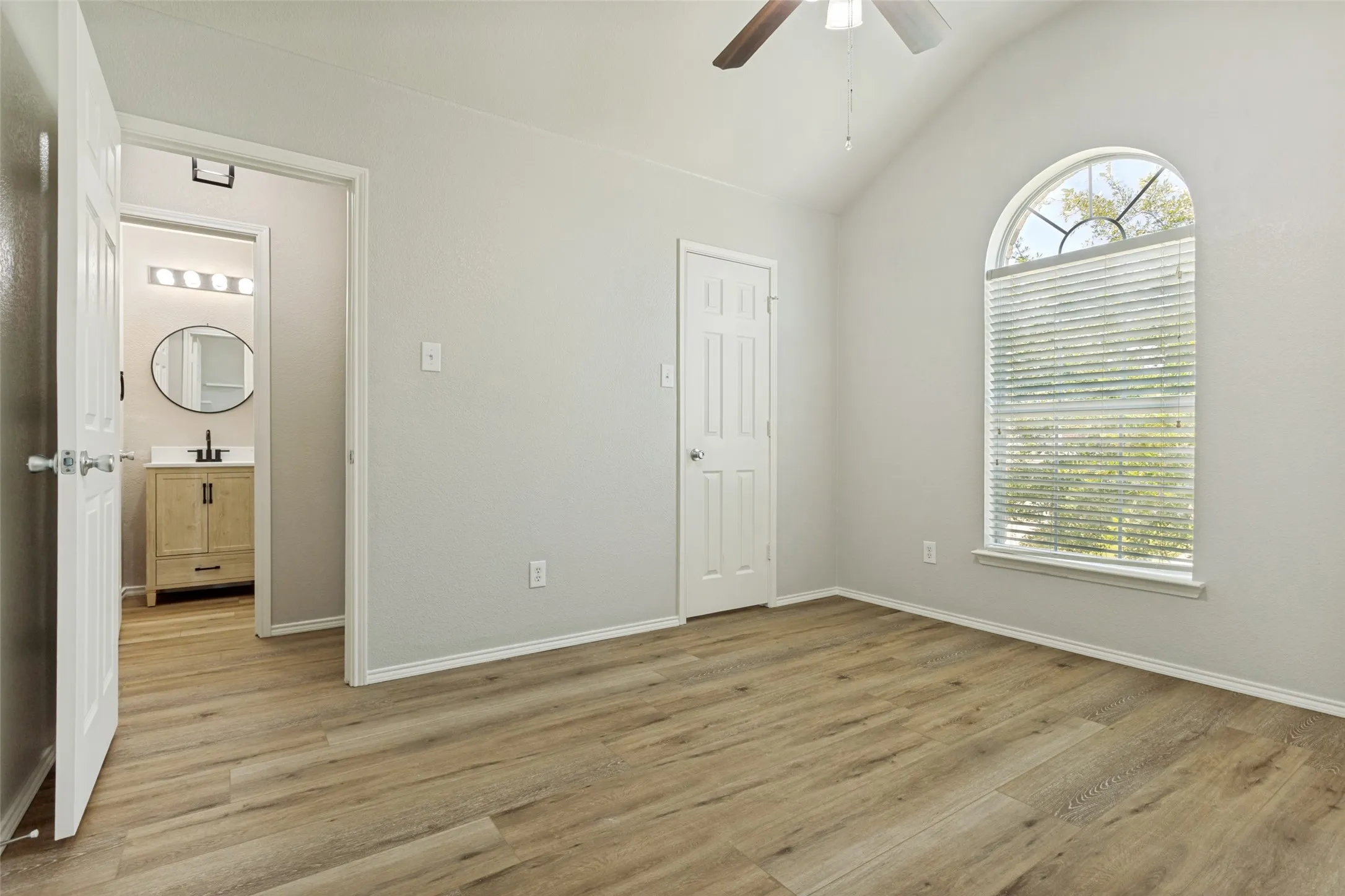 Vaulted ceiling bedroom with wood-finish flooring, a ceiling fan, and an arched window