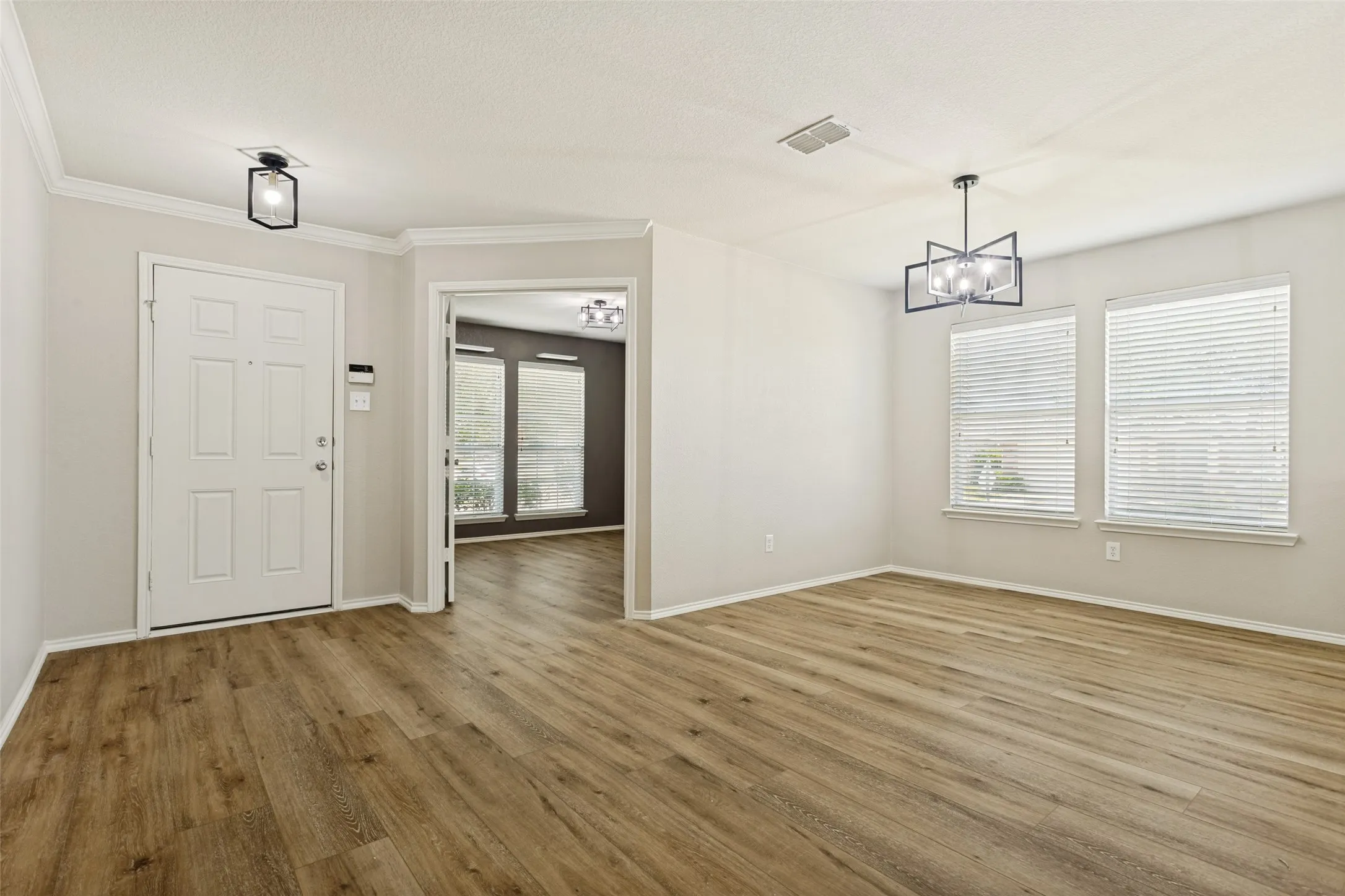 Entryway and room featuring wood-finish flooring, neutral wall tones, crown molding, and modern light fixtures