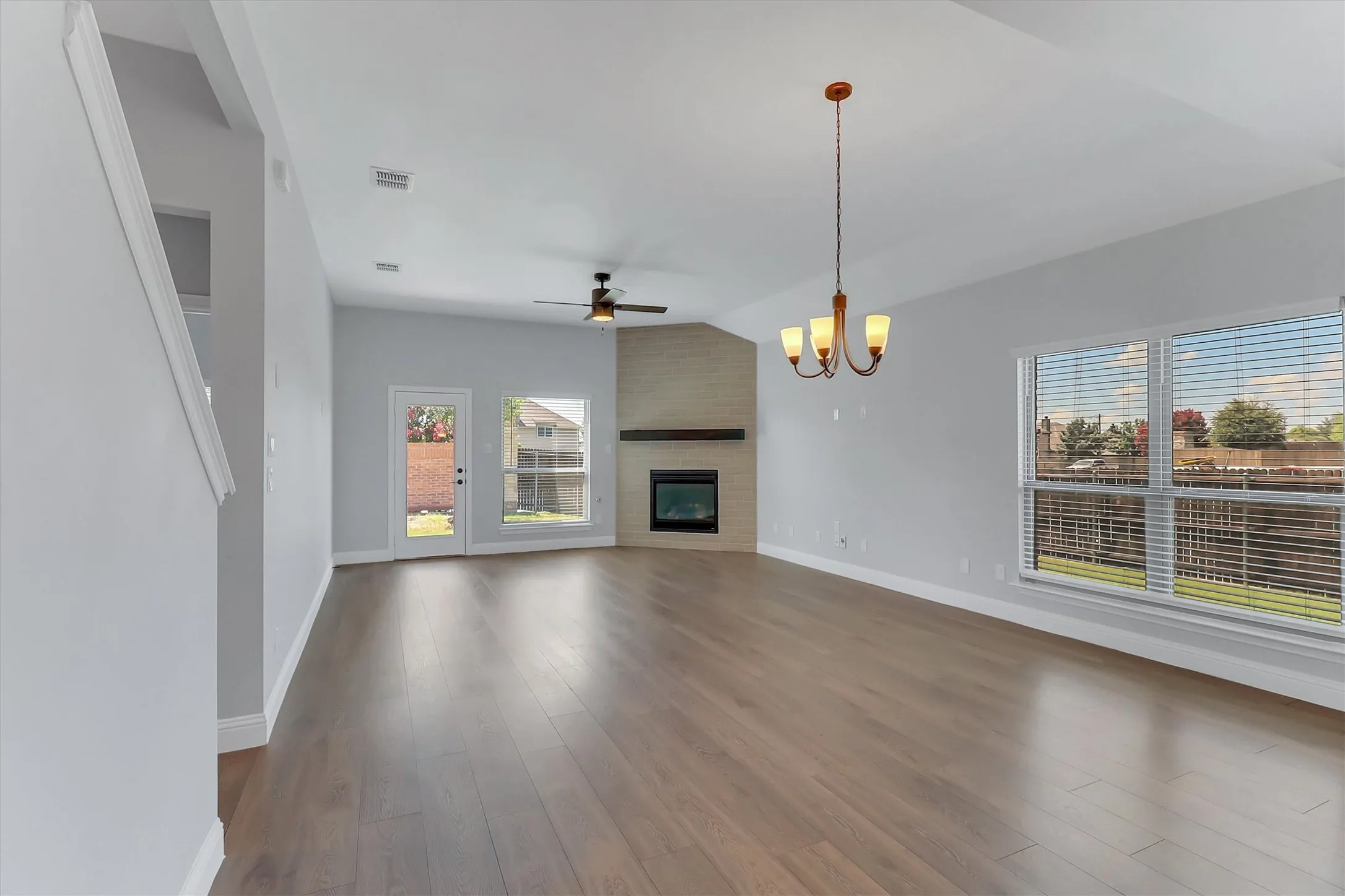 Spacious living area featuring wood-finish flooring, a corner fireplace with a mantel, and a ceiling fan