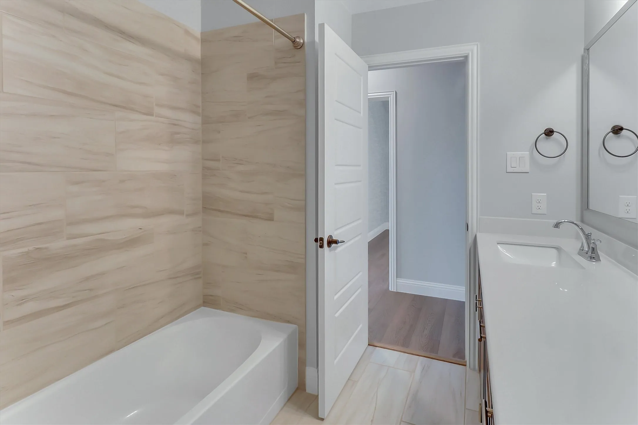 3rd Bathroom Modern bathroom featuring a white bathtub with tile surround, a single vanity with a white countertop and integrated sink, a large wall mirror, and panel doors