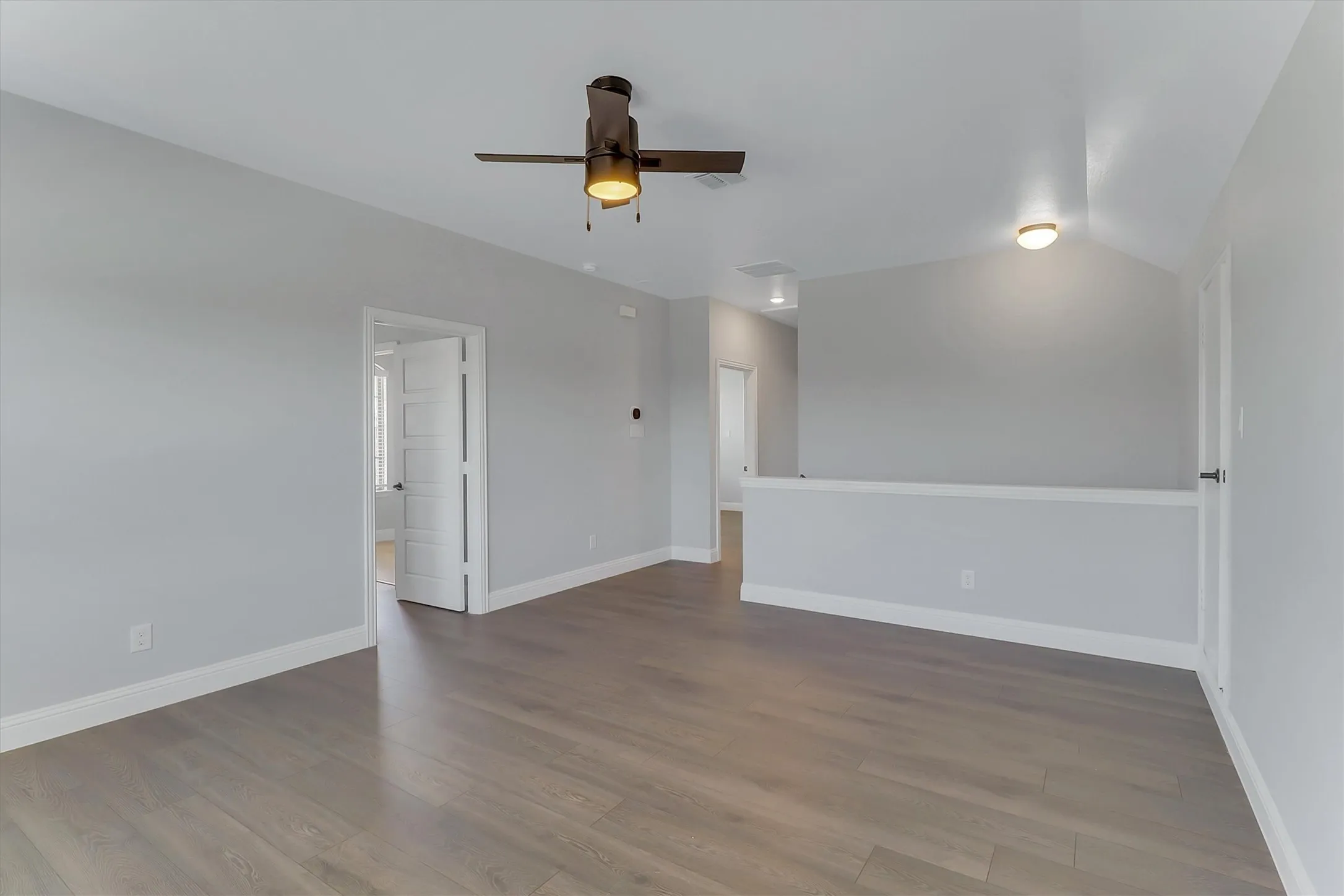 Spacious room featuring wood-finish flooring, light gray walls, white baseboards, and a dark bronze ceiling fan with integrated lighting
