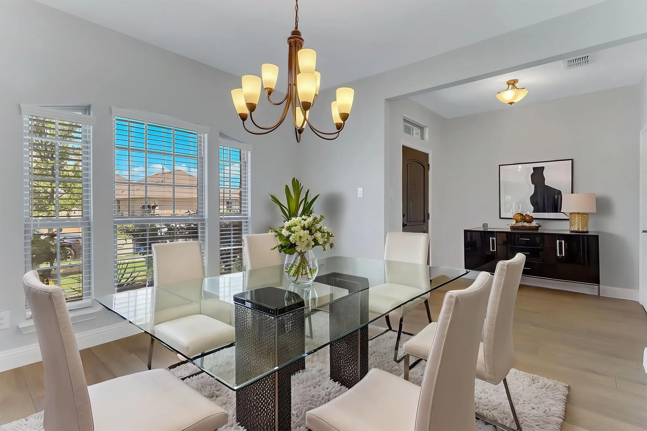 Bright dining area featuring wood-finish flooring, a contemporary chandelier, multiple windows with blinds, a built-in buffet, and a recessed ceiling light fixture. Virtual stage