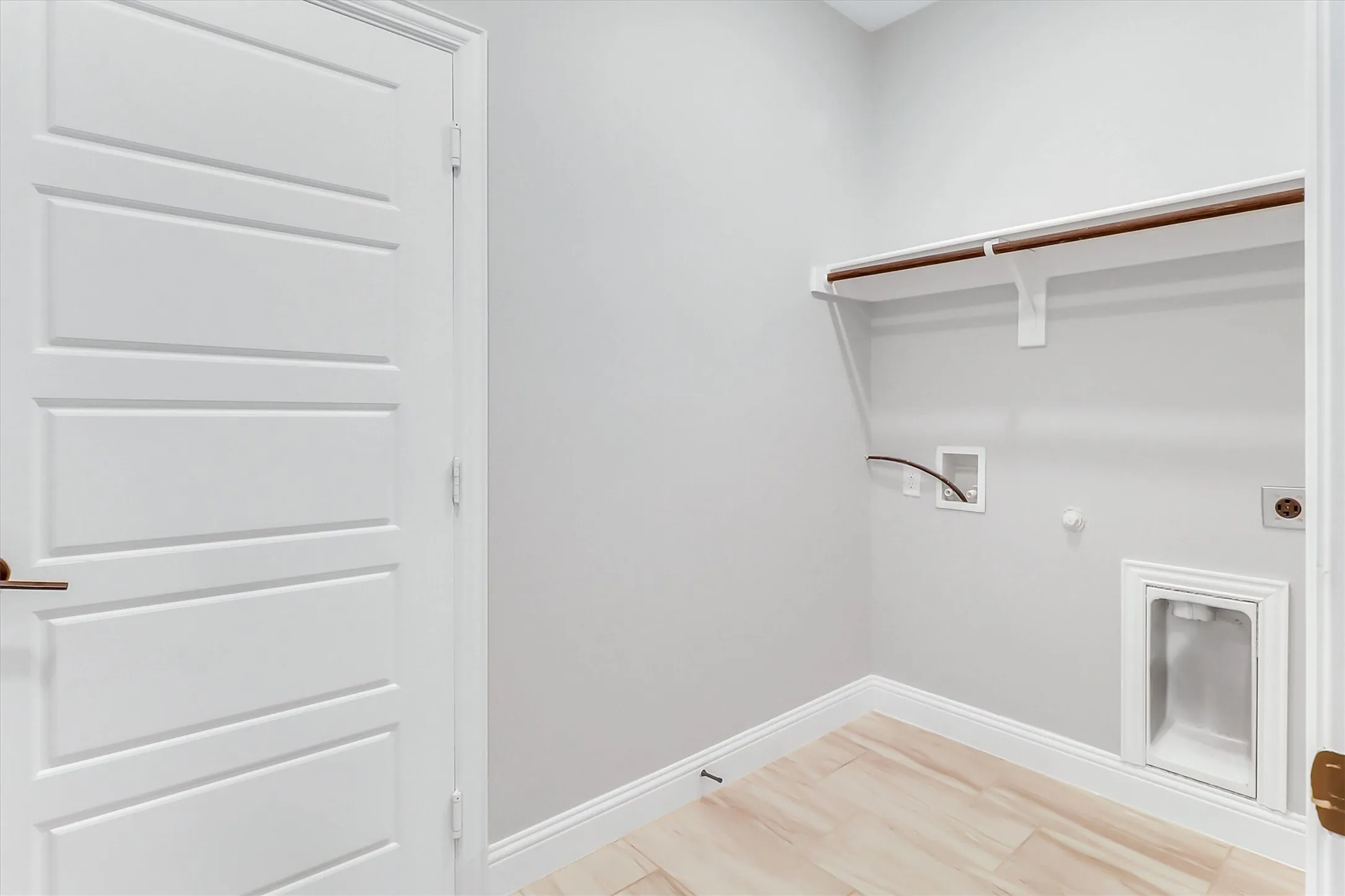 Utility area featuring a white four-panel door with bronze hardware, light wood-finish flooring, white baseboards, and light gray wall paint