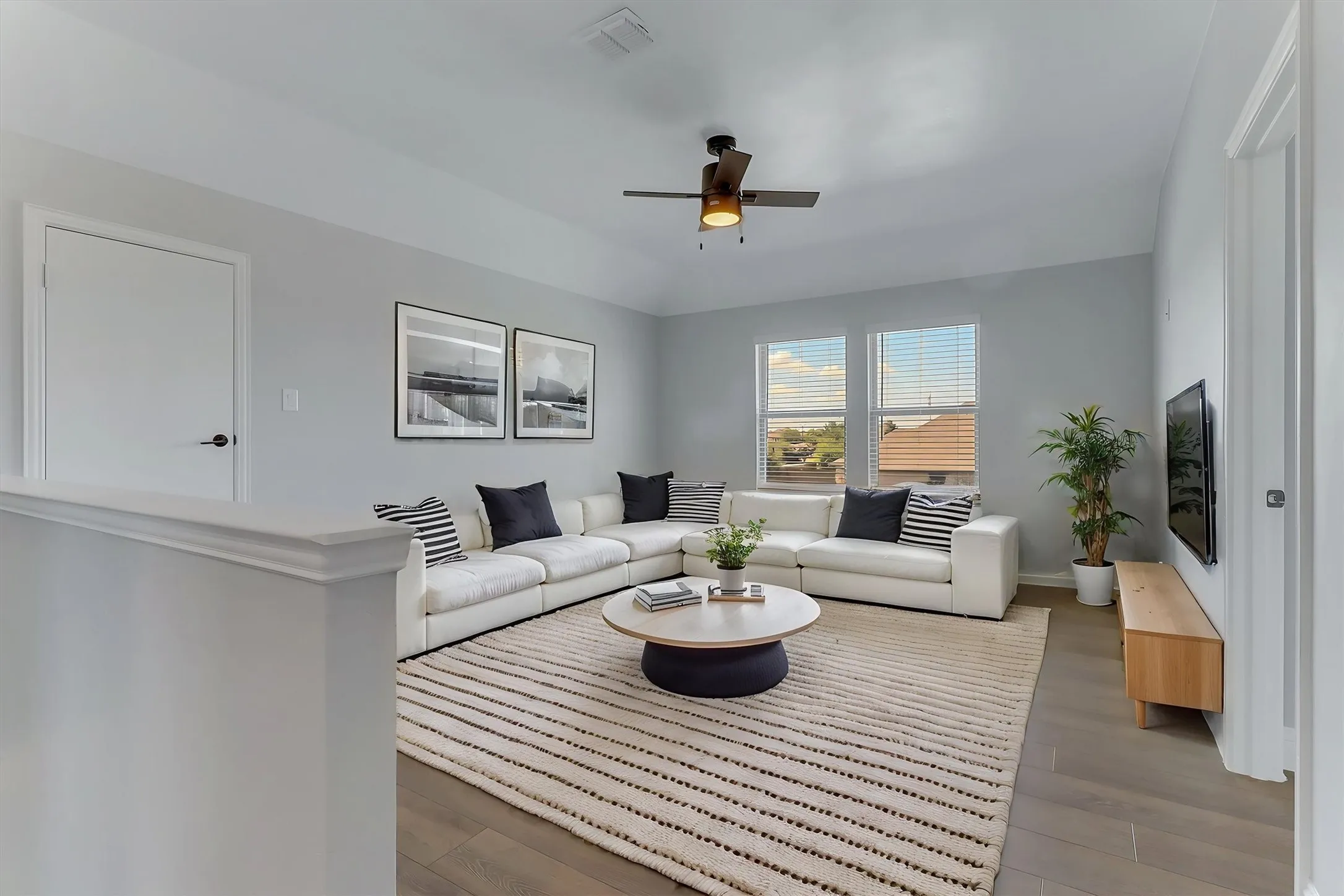 Spacious living area featuring wood-finish flooring, a ceiling fan with integrated lighting, and multiple windows with blinds. Virtual stage