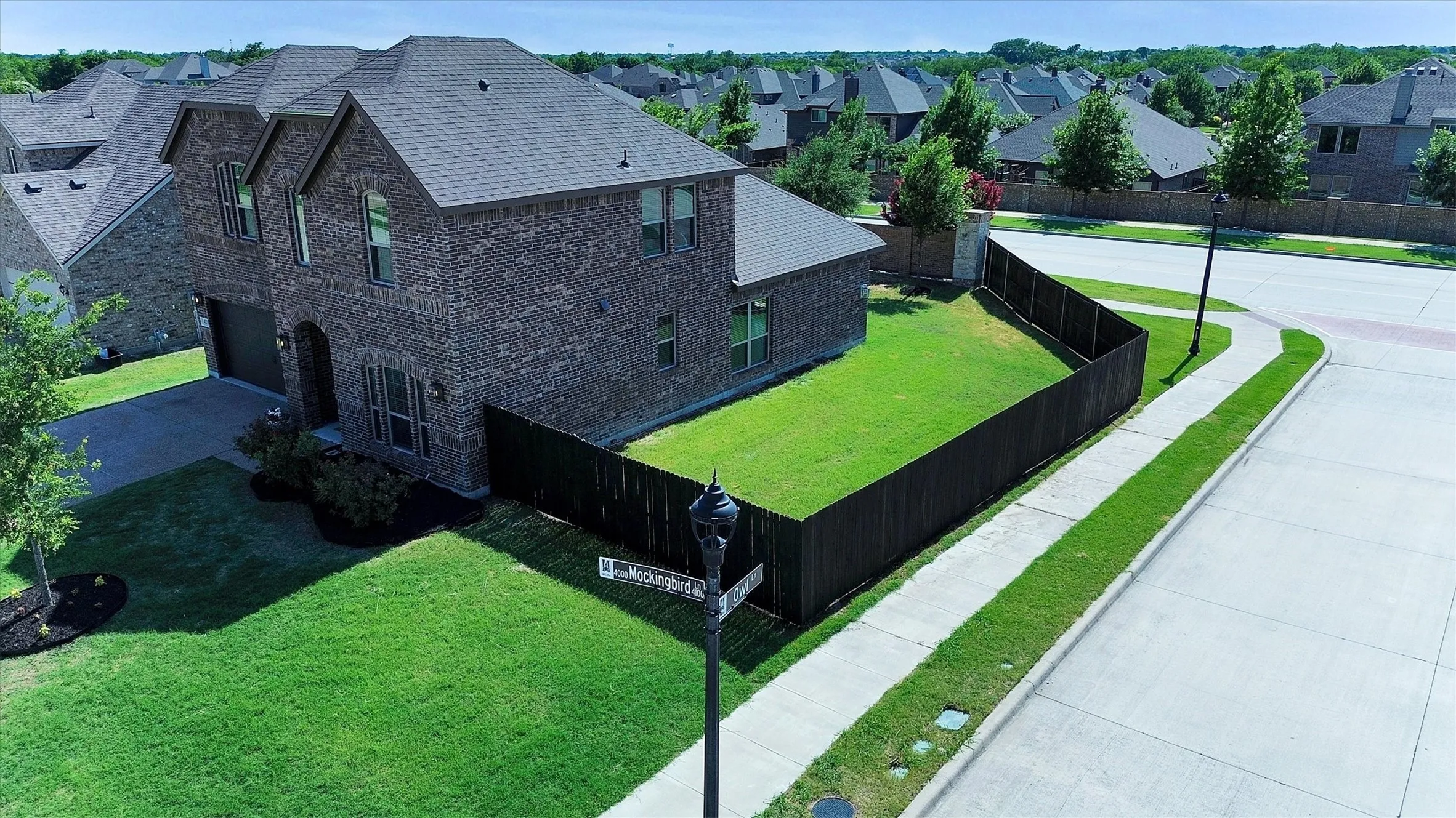 Two-story brick exterior featuring a dark composition shingle roof, attached garage, and a dark wood privacy fence