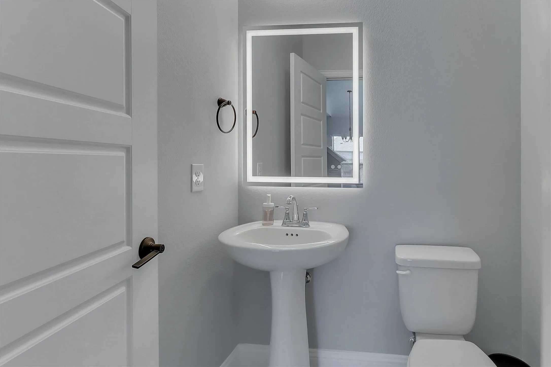 Pedestal sink with chrome faucet, illuminated mirror, and a modern two-panel door with dark bronze hardware