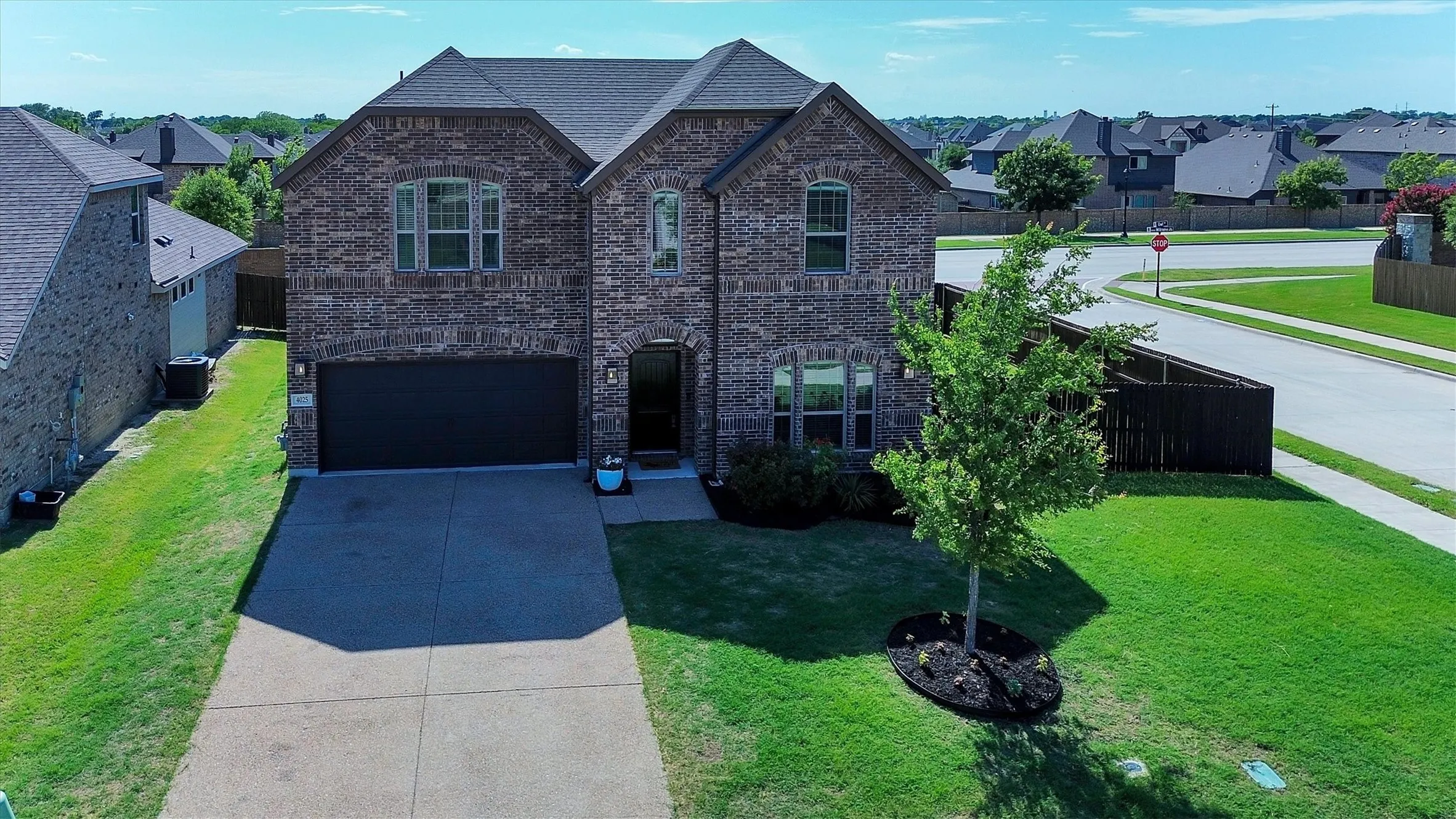 Brick facade home featuring a two-car garage, mature landscaping, dark-framed windows, and a concrete driveway