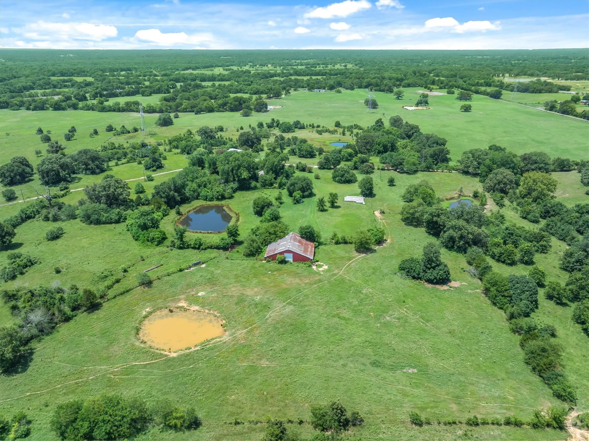 Expansive green acreage featuring a red barn, multiple ponds, and scattered mature trees