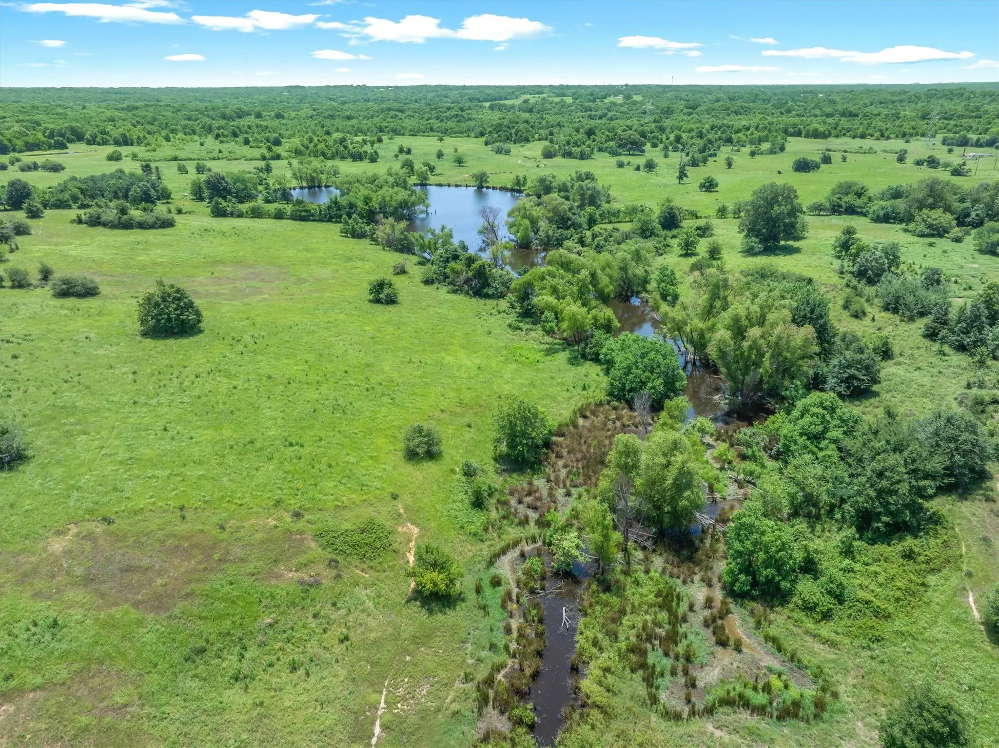 Expansive property featuring varied topography, including open fields, wooded areas, and a visible water body