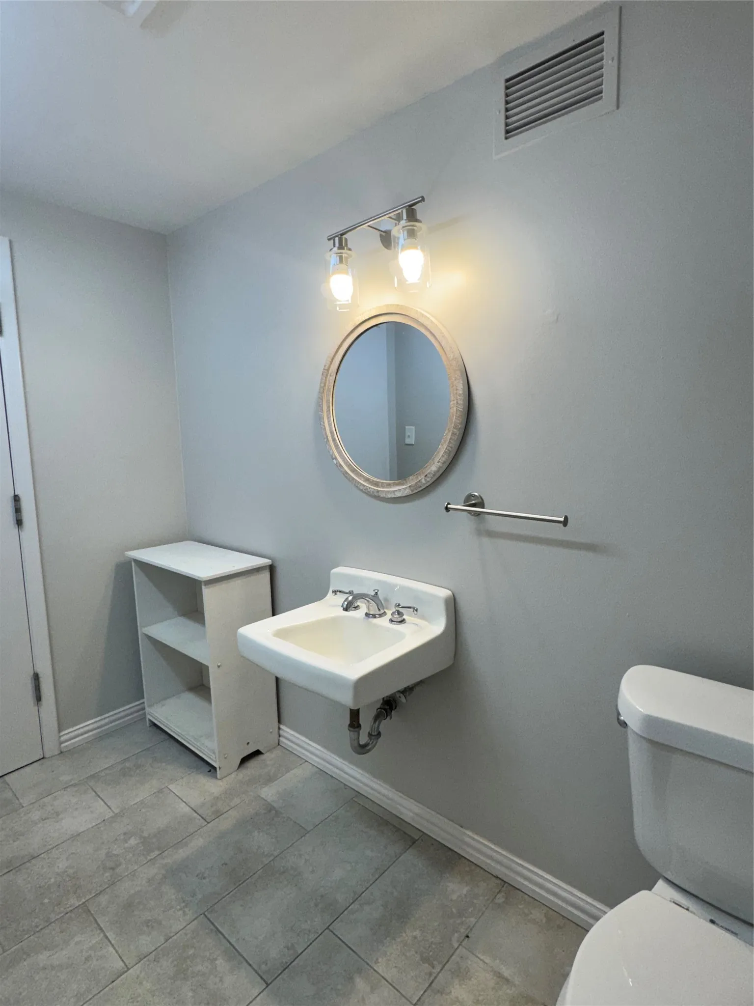 Pedestal sink with chrome faucet, complemented by a round framed mirror and a two-bulb vanity light