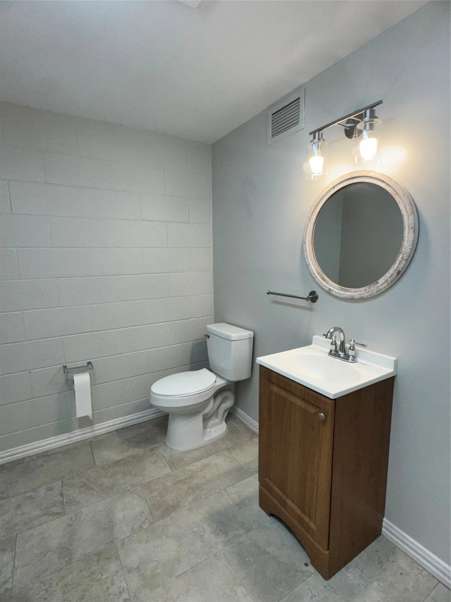 Bathroom featuring a wood-finish vanity with an integrated sink, a circular mirror, and a two-light vanity fixture