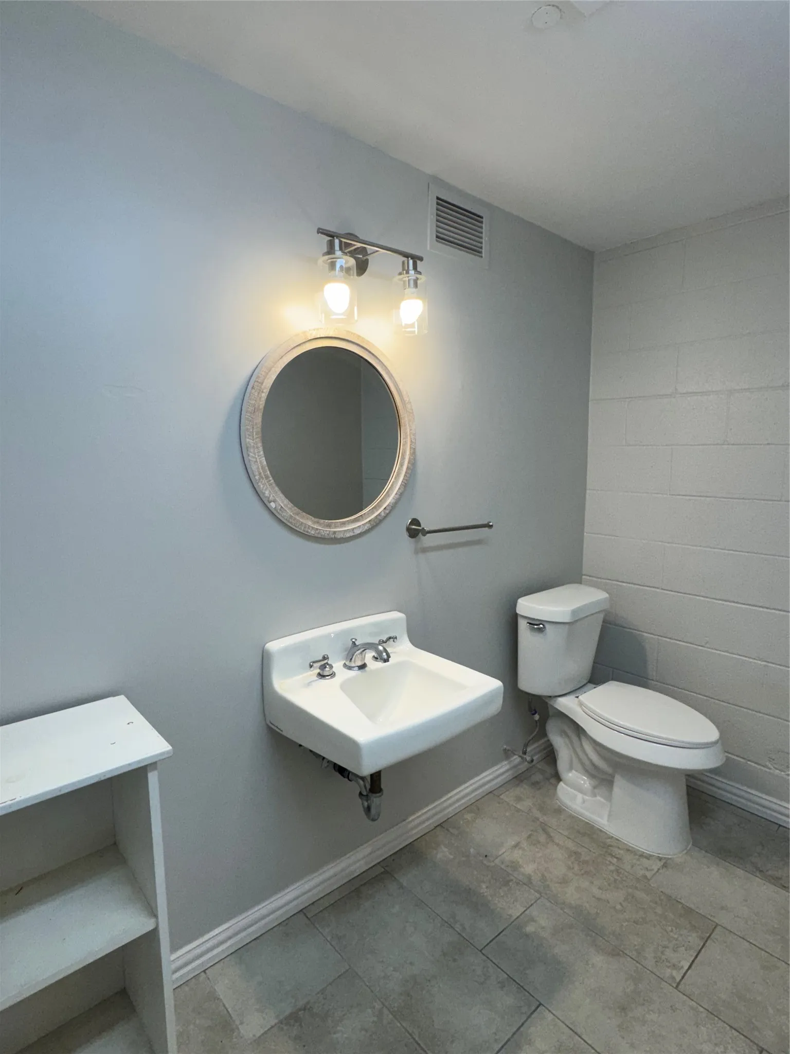 Modern bathroom with a wall-mounted sink, round mirror, and tile flooring