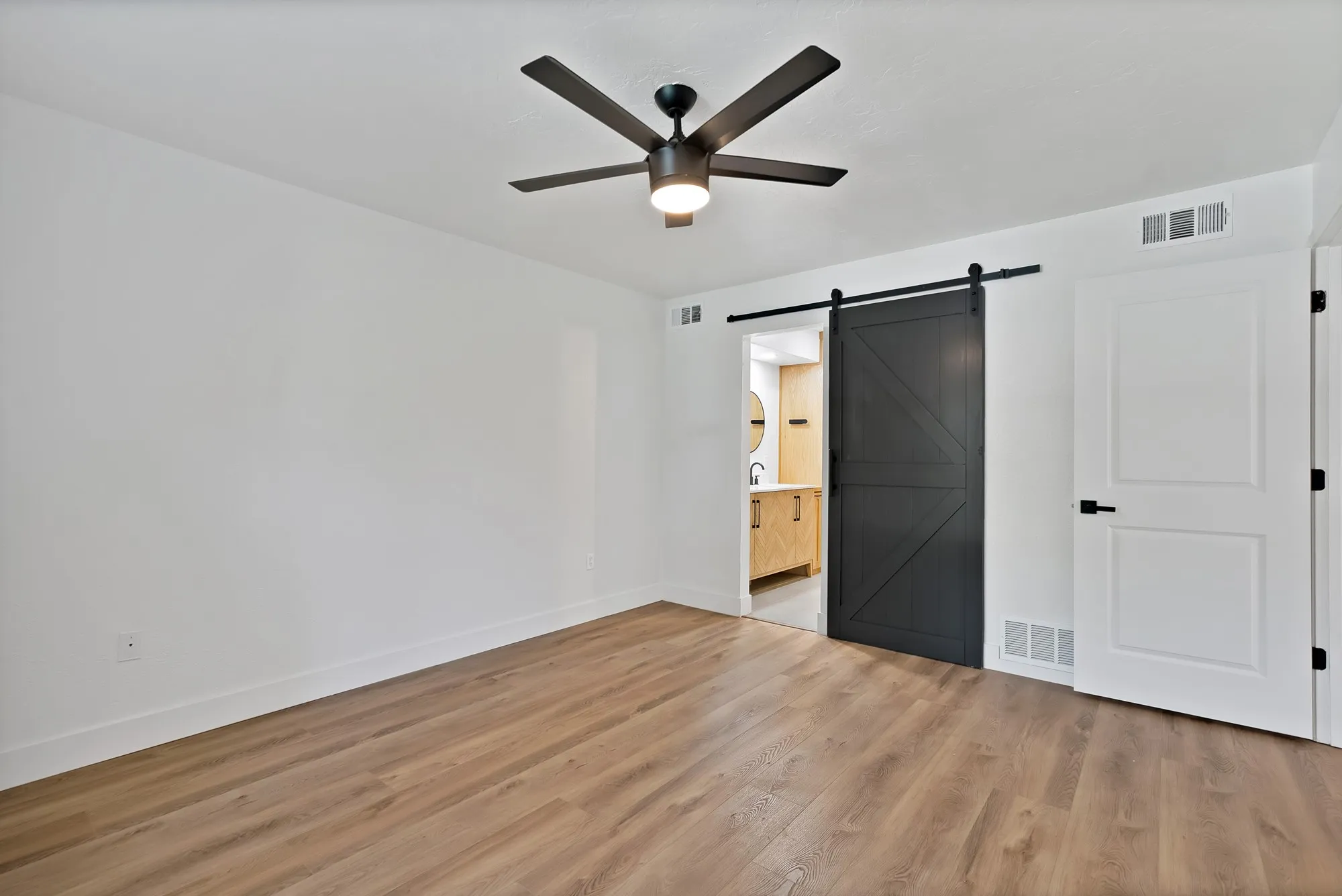 Spacious room featuring wood-finish flooring, white walls, and a black ceiling fan with integrated lighting