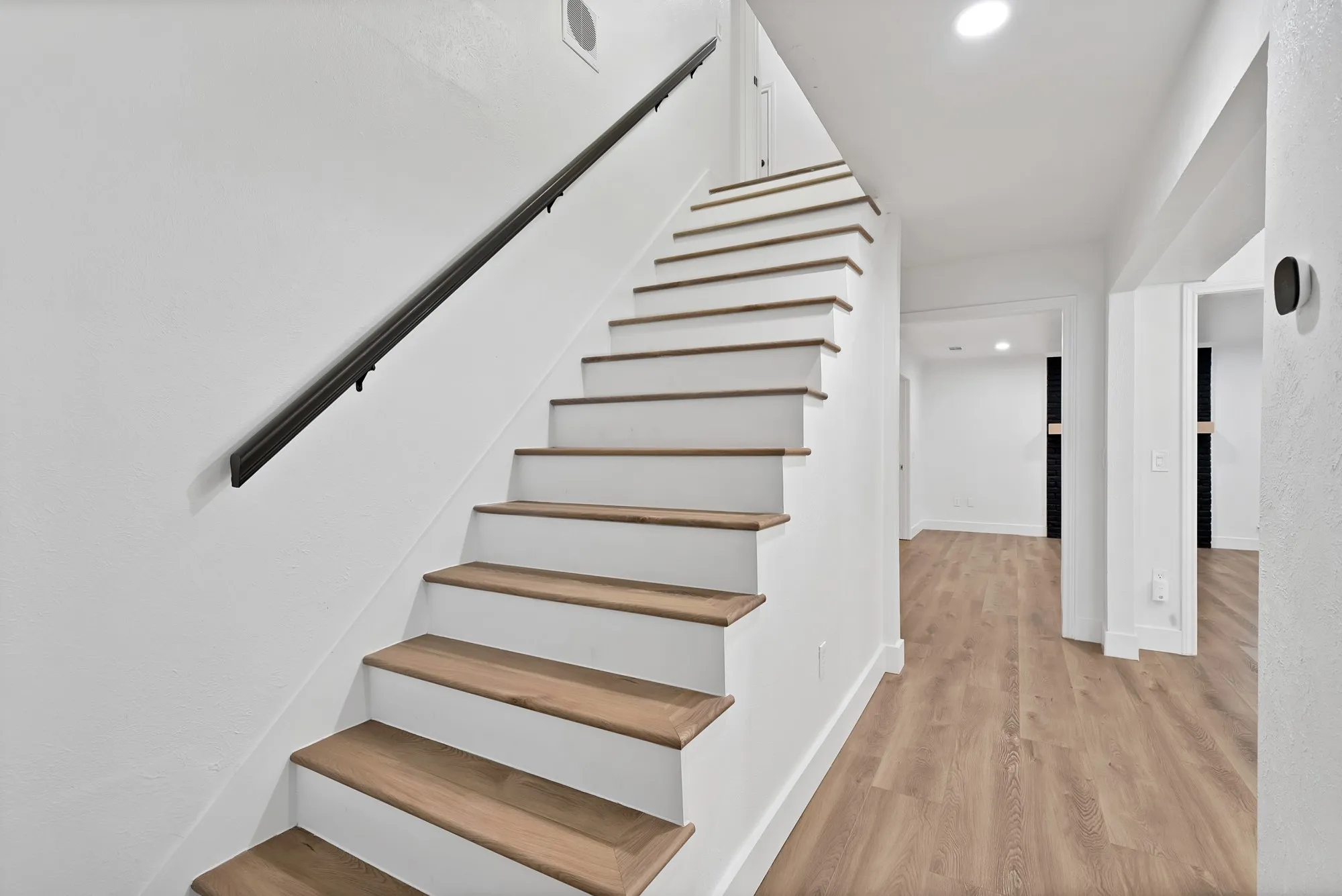 Staircase featuring wood-finish treads and white risers with a black wall-mounted handrail