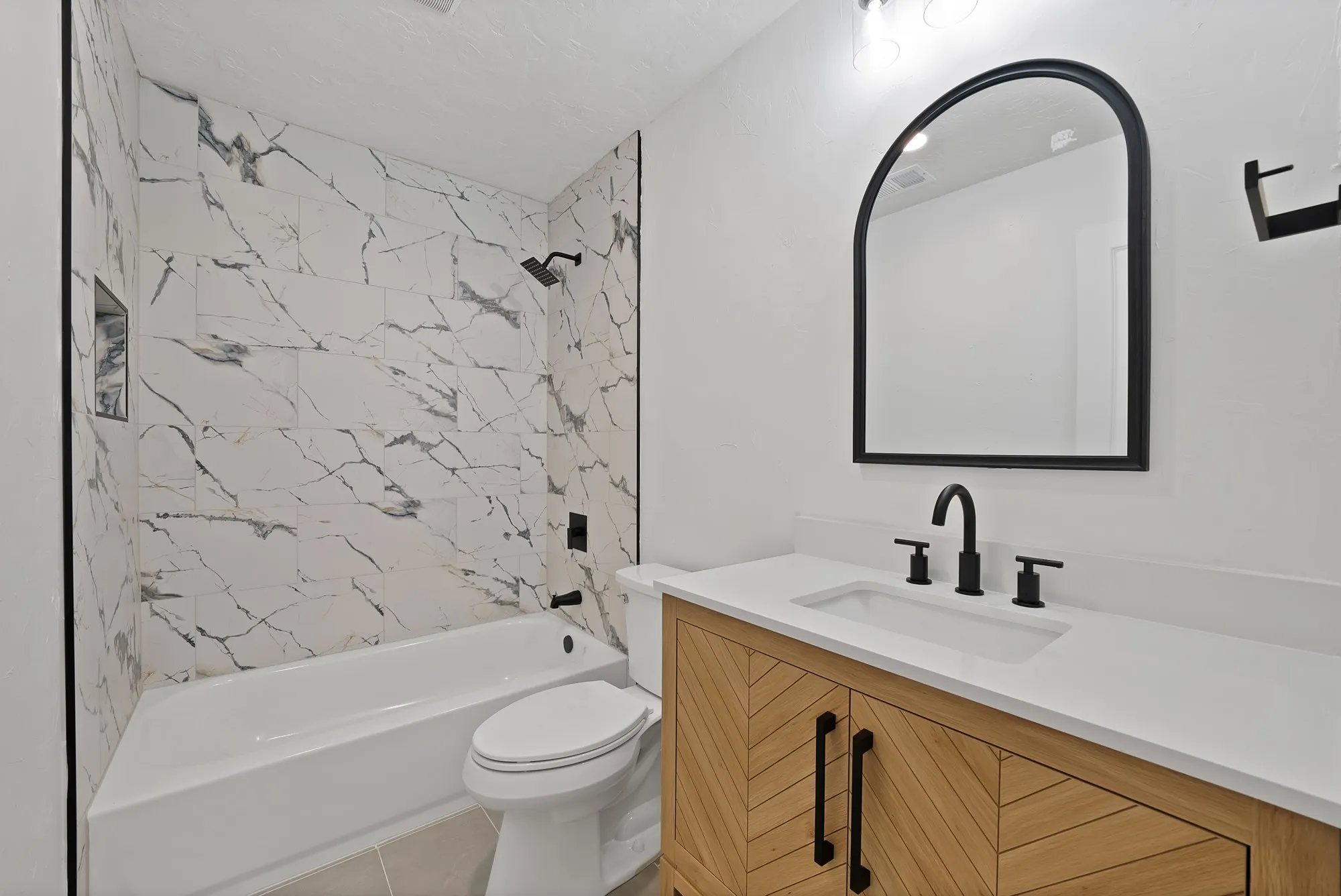 Modern bathroom featuring a white bathtub with marble-look tile surround, black shower fixtures, and a recessed shower niche