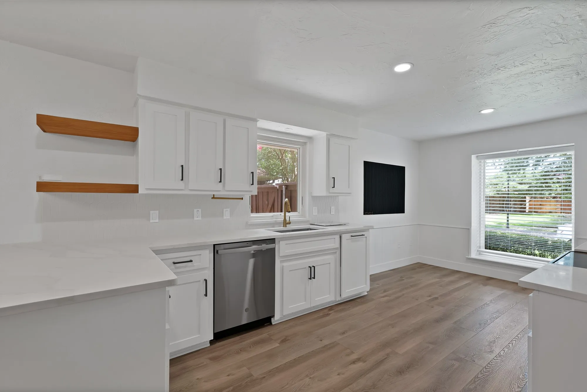 Kitchen featuring white shaker cabinetry with black hardware, light-toned countertops, a stainless steel dishwasher, and wood-finish flooring