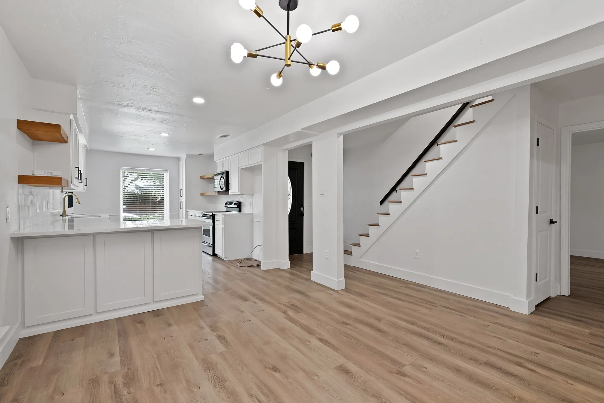 Open-concept main living space featuring wide-plank wood-finish flooring, a modern sputnik chandelier, and a white kitchen with shaker cabinetry