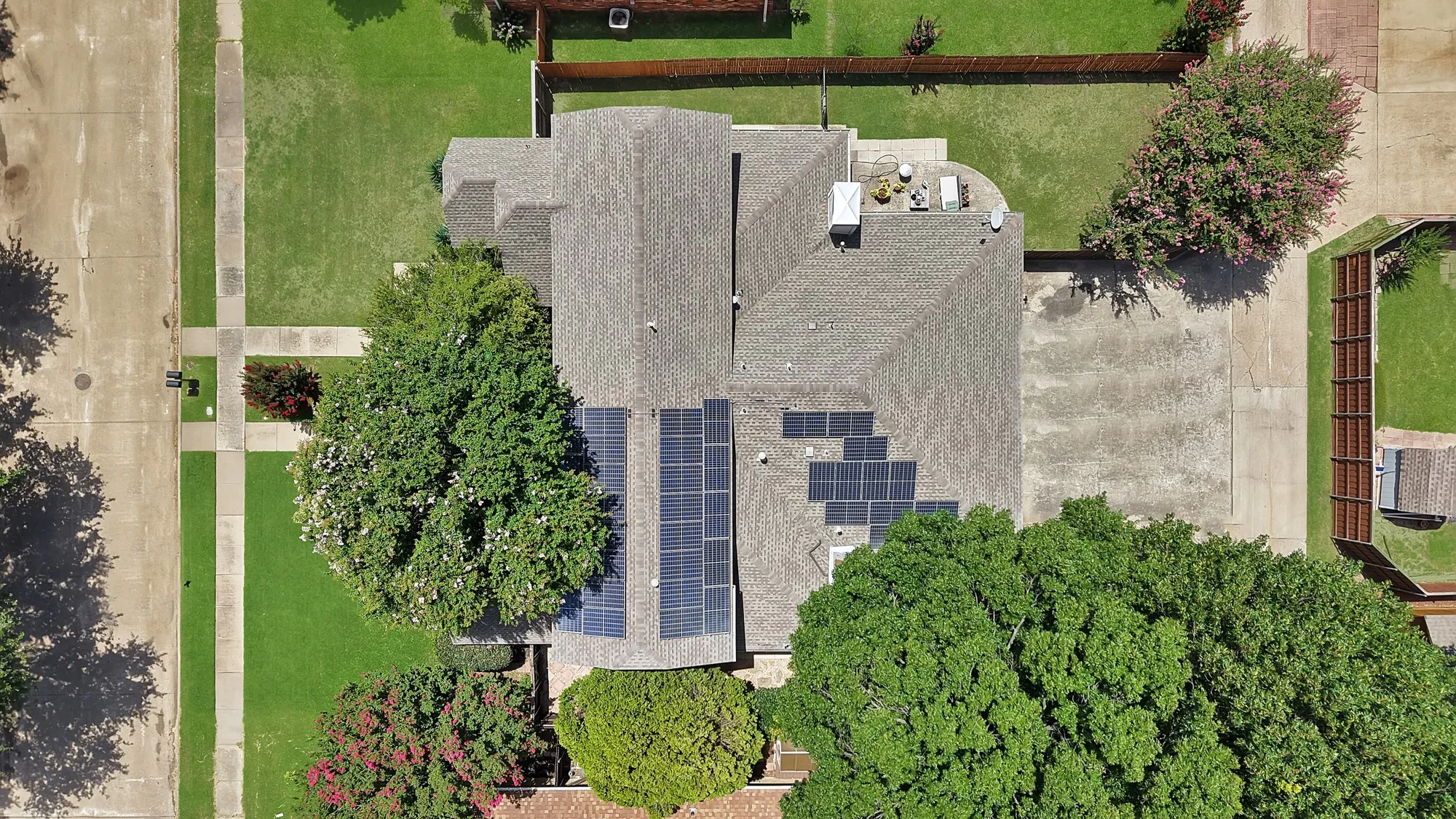 Residential property featuring a shingled roof, multiple solar panel arrays, and a concrete patio