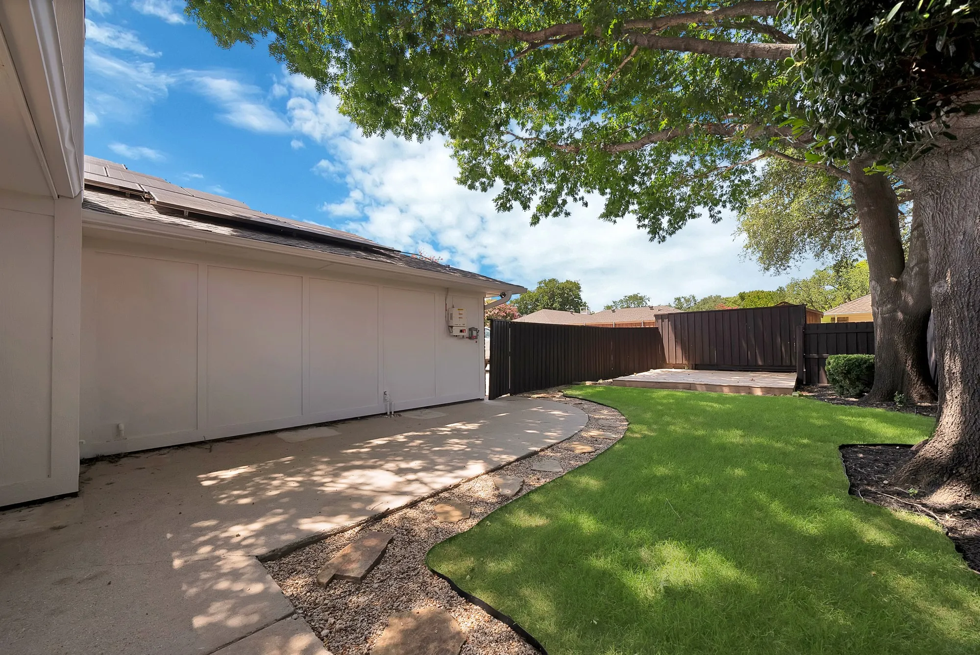 Private backyard featuring a wooden privacy fence, a raised wooden deck, and a mature shade tree