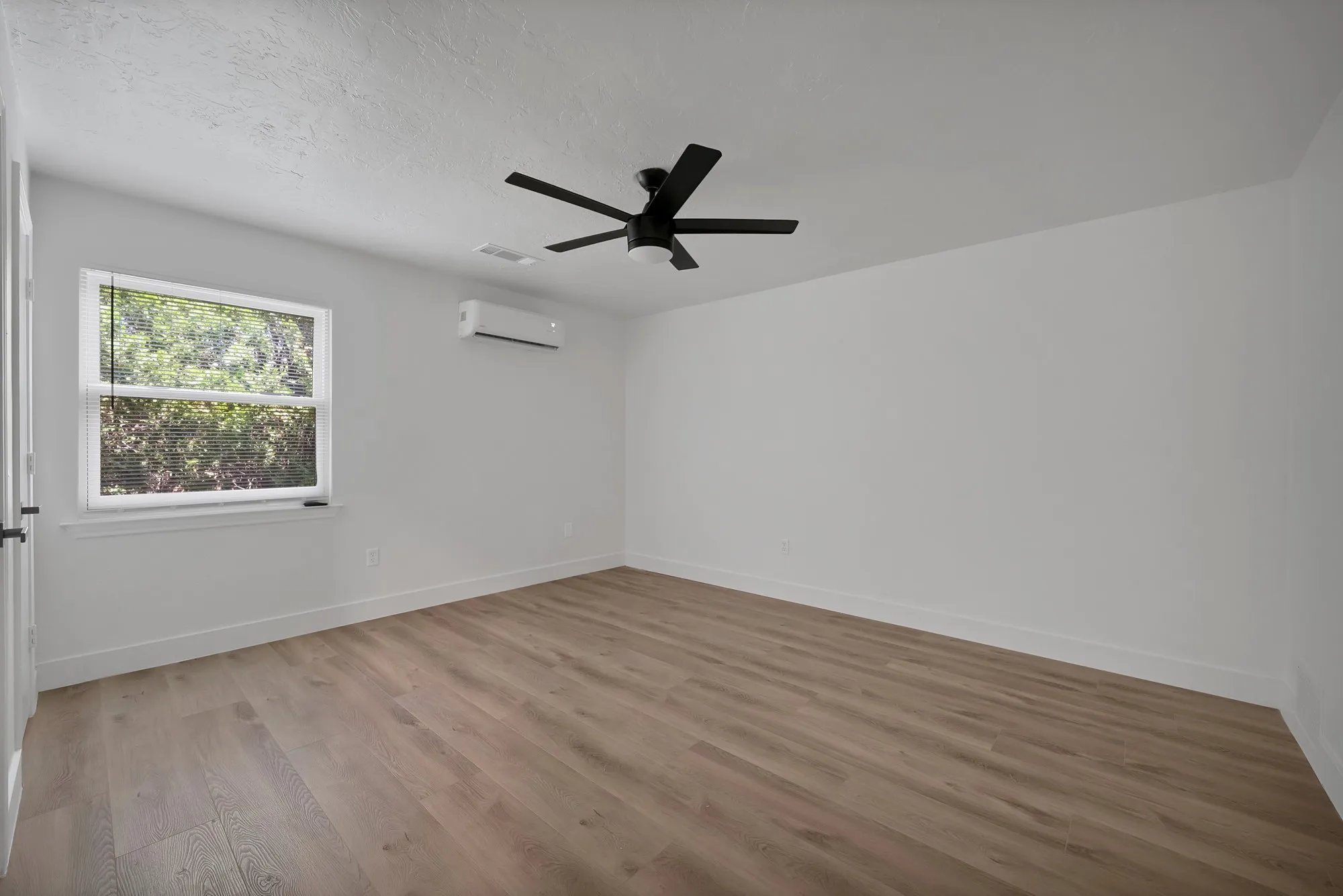 Spacious room featuring wood-finish flooring, a contemporary ceiling fan, and an individual wall-mounted climate control unit