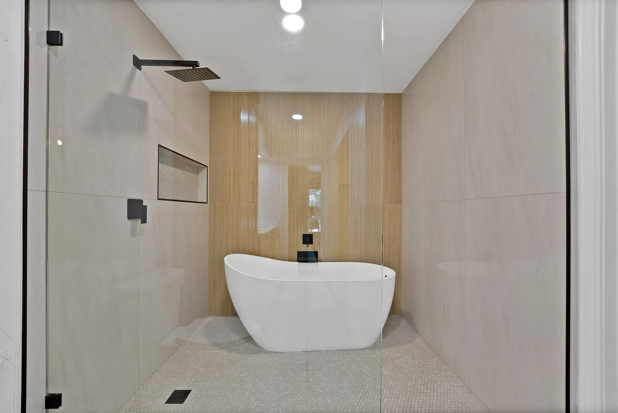 Walk-in shower enclosure with a freestanding soaking tub, matte black fixtures, integrated wall niche, and large format wall tiling