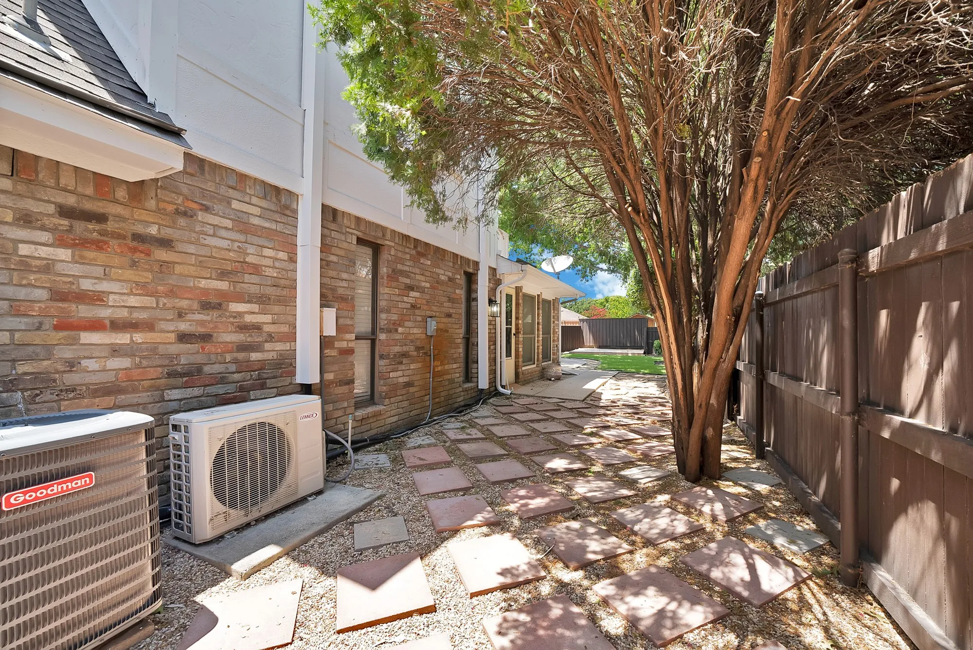 Side yard featuring a stone paver pathway, gravel ground cover, mature tree, and a wood privacy fence