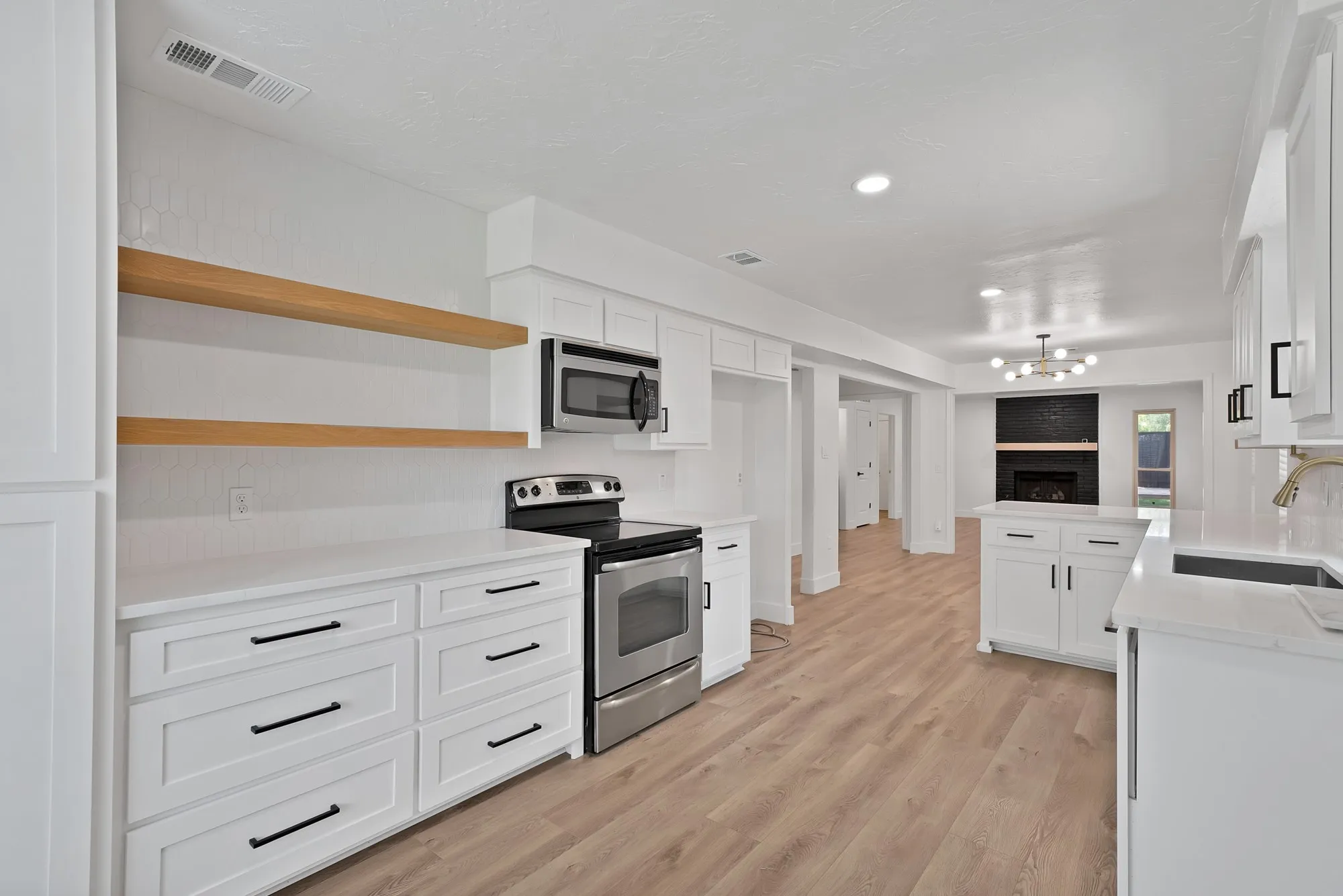 Open-concept kitchen featuring white cabinetry with black hardware, stainless steel appliances, wood-finish flooring, and white countertops