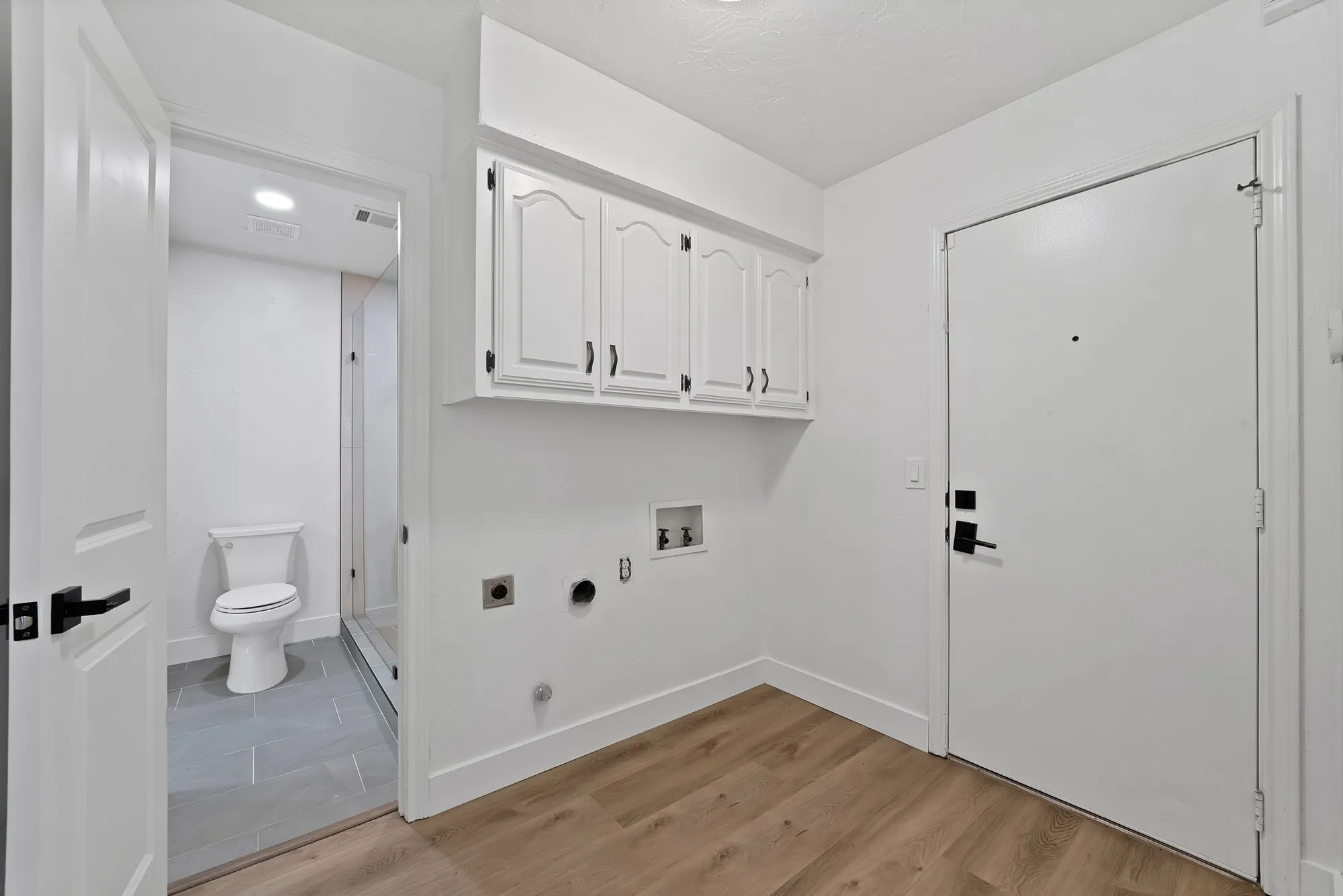 Utility area featuring wood-finish flooring, white cabinetry with black hardware, and laundry hookups