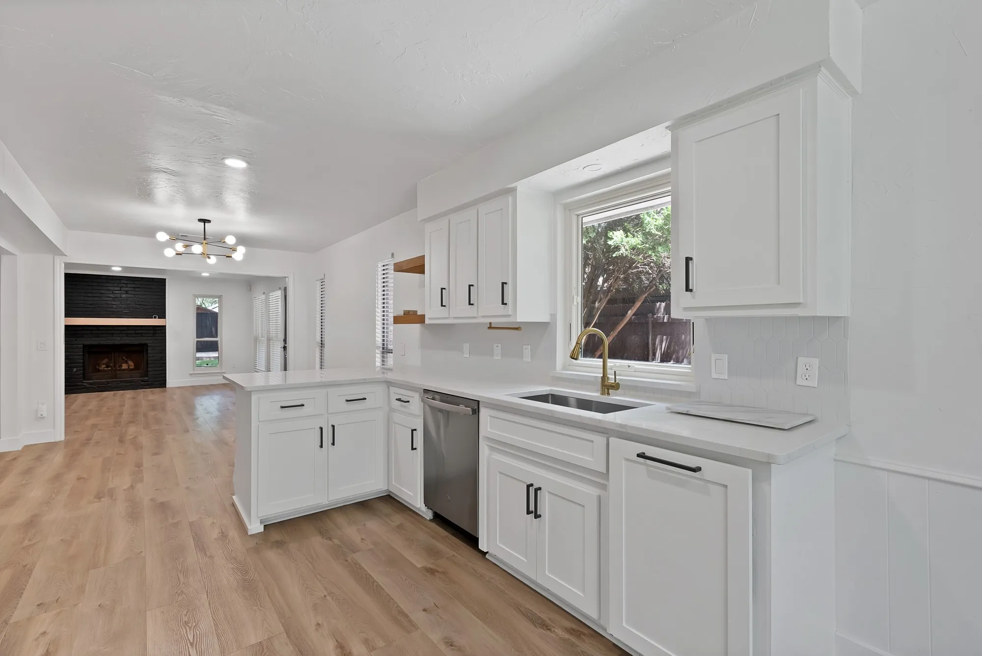 Bright kitchen featuring white shaker cabinetry, stainless steel dishwasher, and a gold-finish faucet
