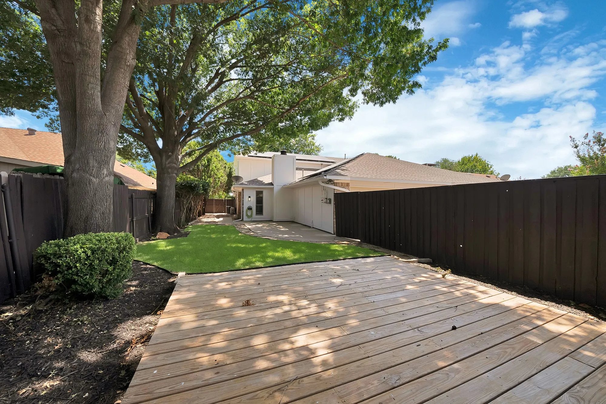 Expansive backyard featuring a wood deck, artificial turf, and mature trees providing natural shade