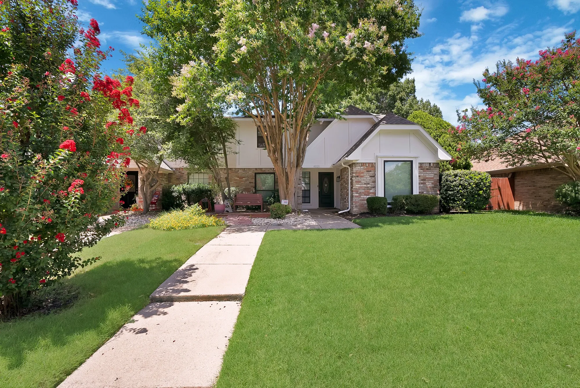 Traditional-style residence featuring a brick and siding exterior, established landscaping, and a concrete pathway