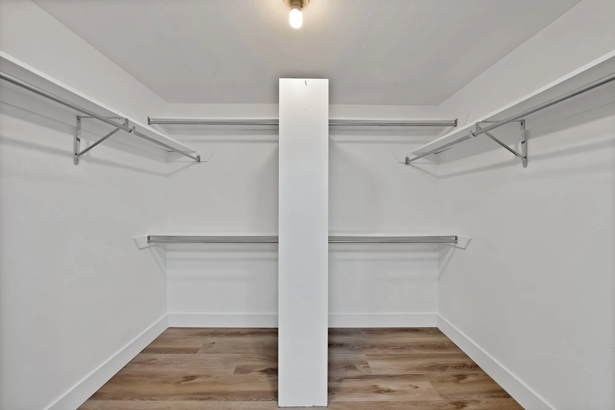 Walk-in closet featuring wood-finish flooring, white baseboards, white walls, multiple hanging rods, and white shelving
