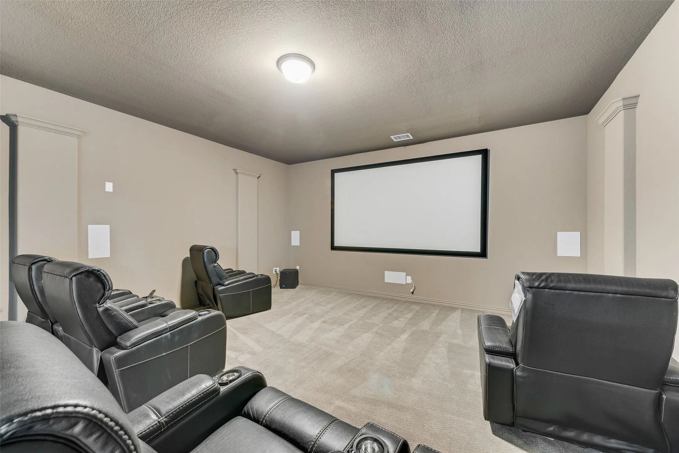 Dedicated media room featuring a large projection screen, wall-mounted speakers, and recessed lighting