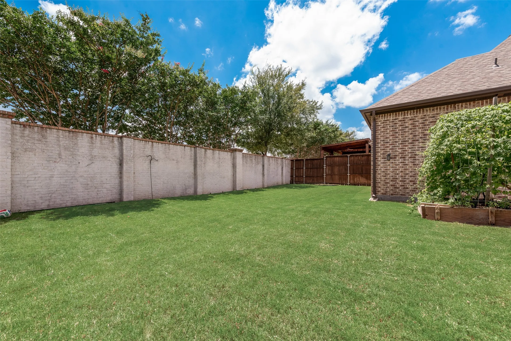 Expansive green lawn framed by a concrete block wall and mature trees