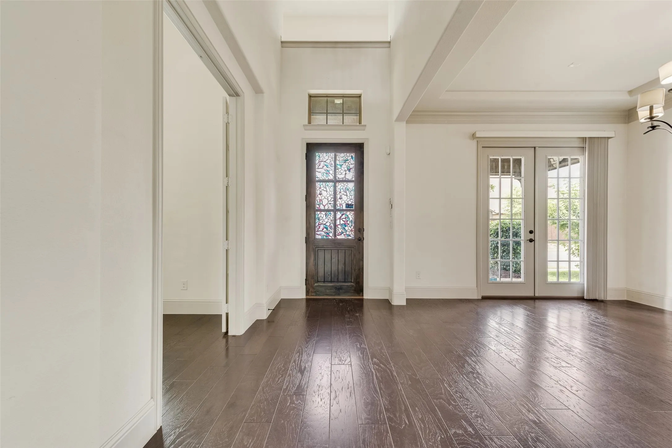 Spacious room featuring dark wood-finish flooring, white walls, and high ceilings with decorative beams