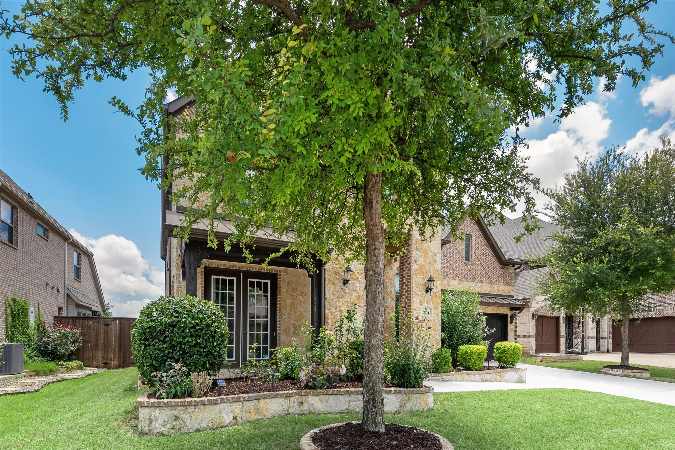 Stone and brick facade featuring wood-framed double doors, gabled roofline, and integrated outdoor lighting