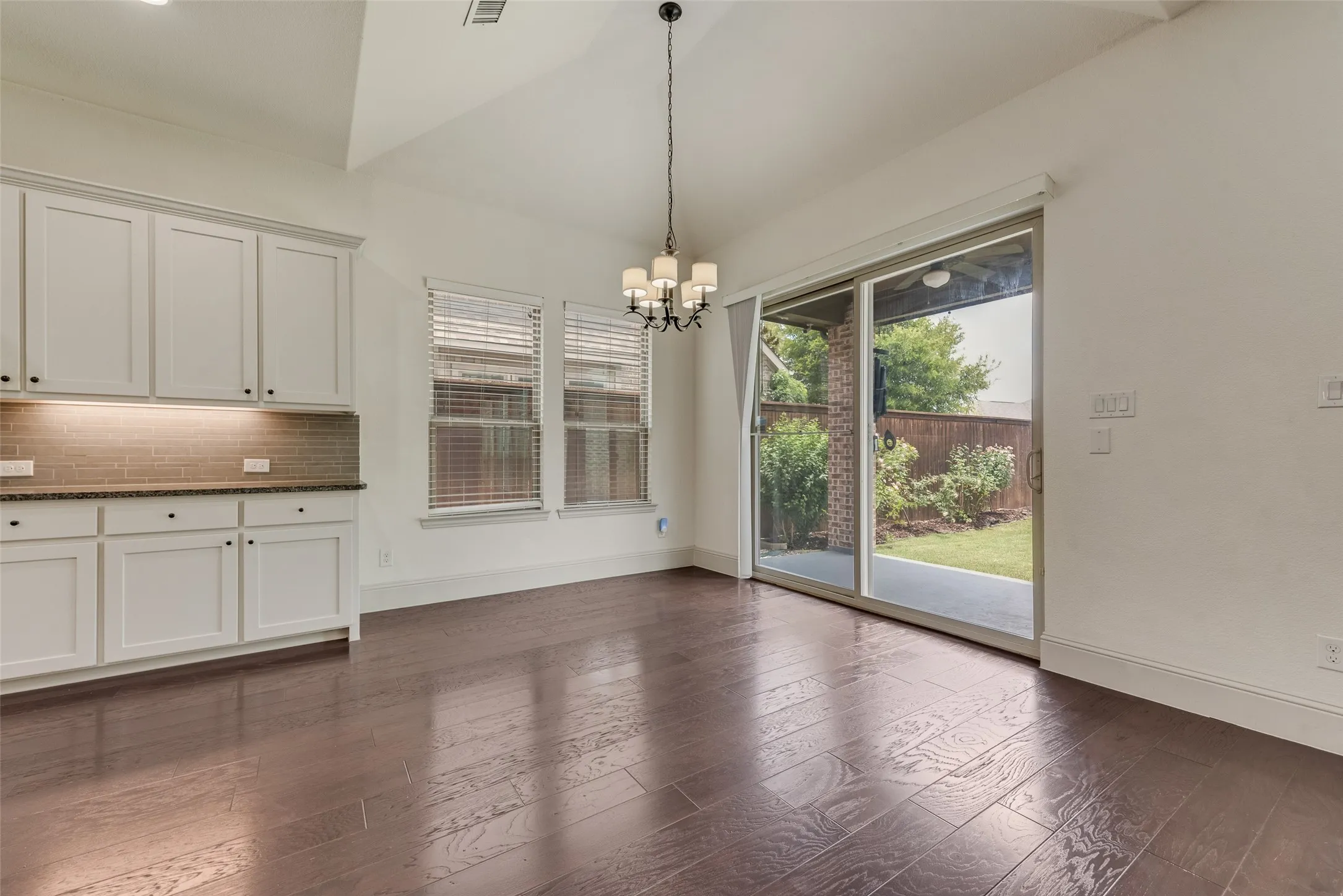 Spacious room featuring dark wood-finish flooring, white cabinetry with dark hardware, and a tile backsplash