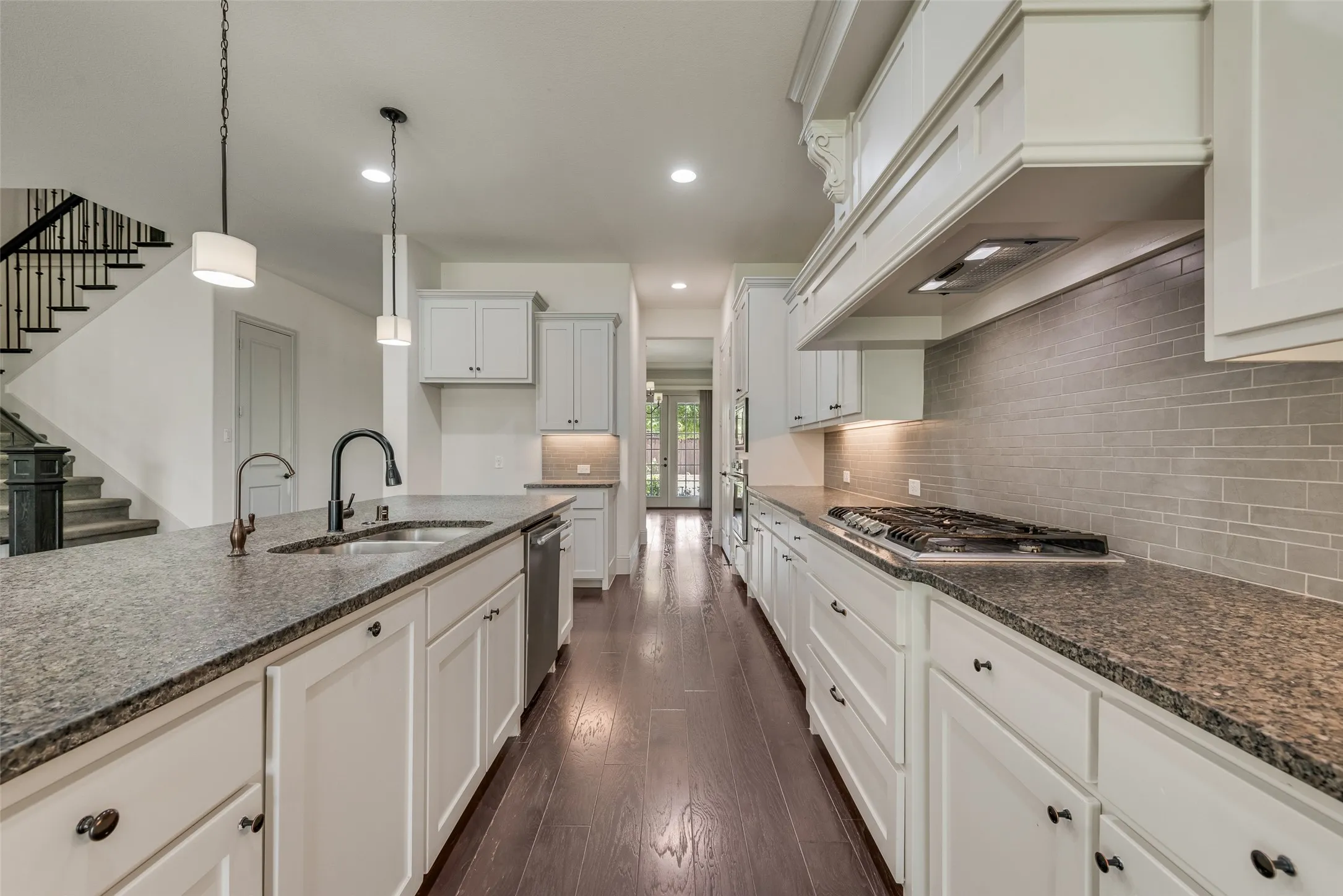 Galley kitchen featuring dark wood-finish flooring, white cabinetry with dark hardware, and speckled countertops