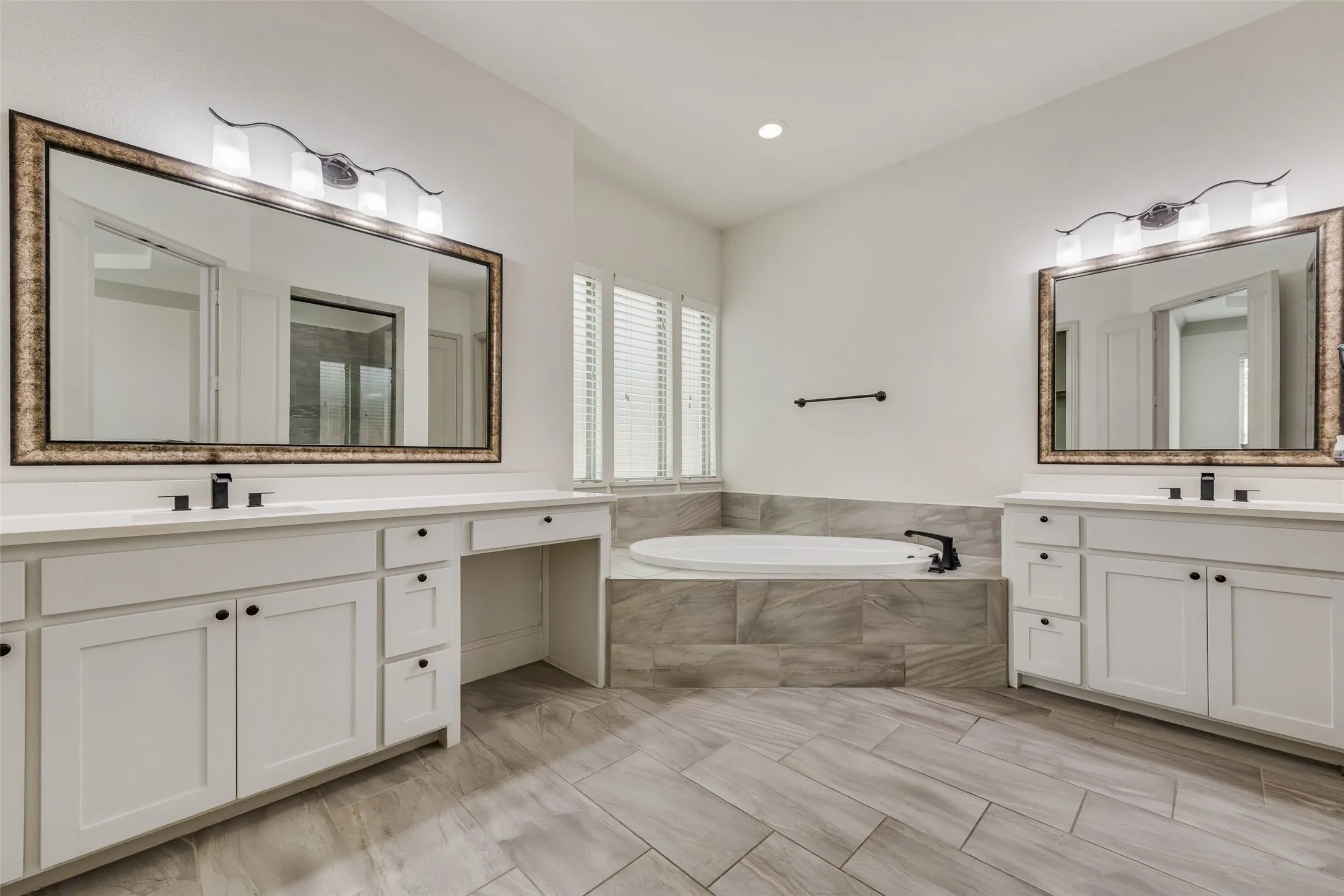 Dual vanity with white cabinetry and integrated sinks, complemented by a corner soaking tub with tiled surround